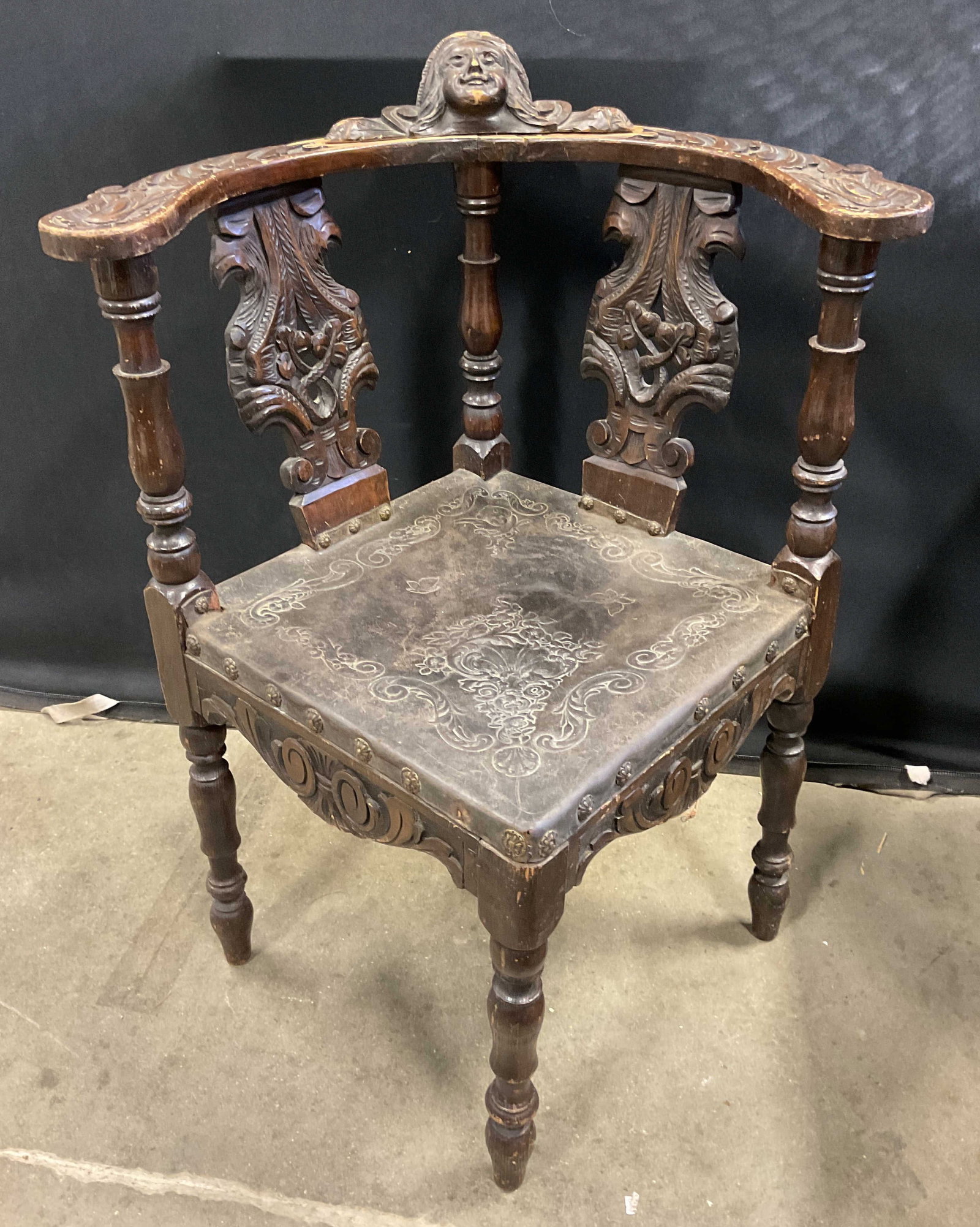 Antique Carved Wood Leather Corner Armchair: Antique carved wood corner armchair with leather seat pad. Ornately carved wood frame with mascaron motif and tooled scroll pattern leather. Measures approx 29 x 24.5 x 35 inches. Wear including scrat