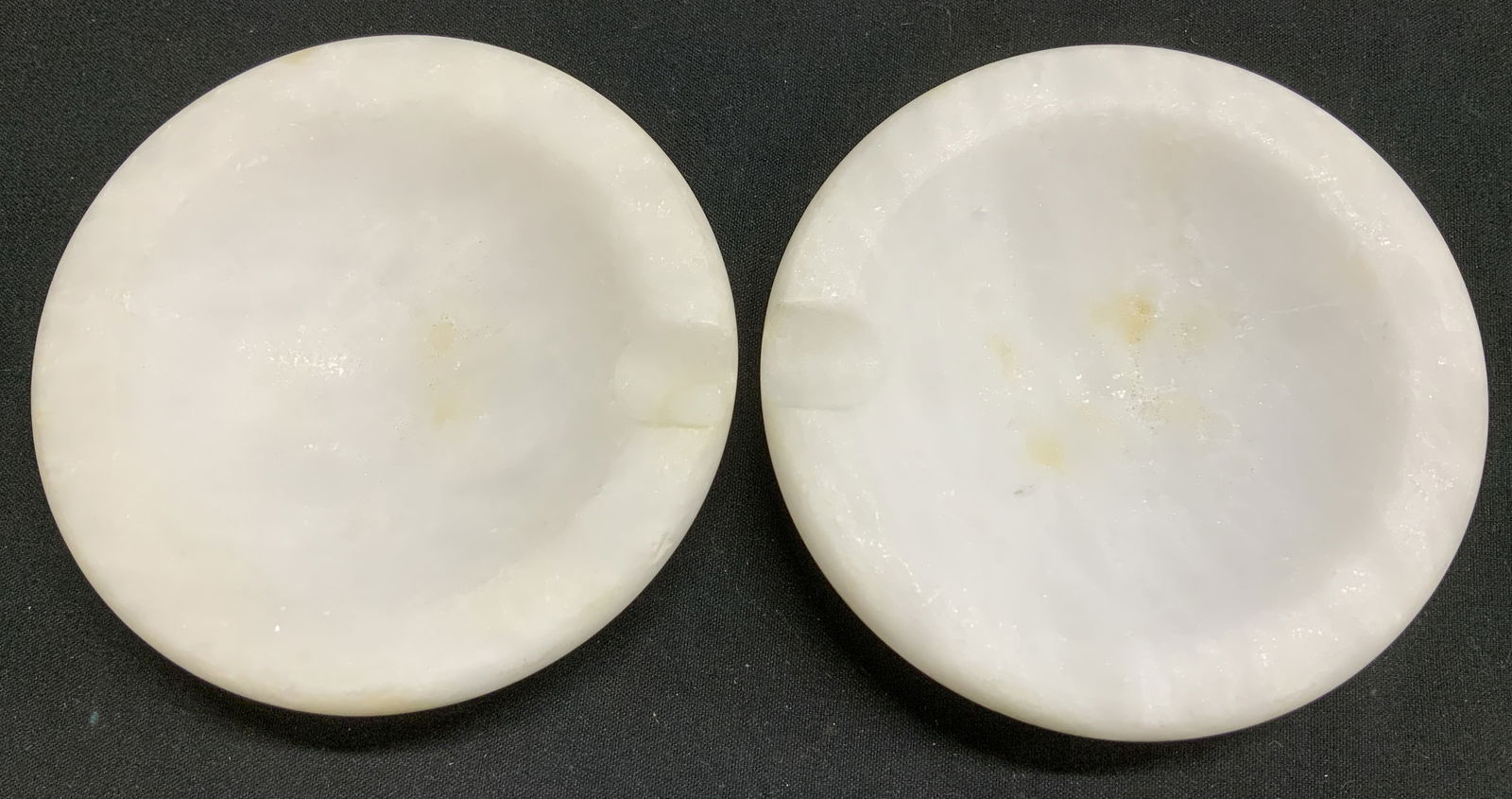 Set 2 Carved White Stone Ashtrays ITALY: Round ashtrays w visible indentation for cigar rest. Carved stone, possible alabaster. Signed & marked on underside. Reads, MADE IN ITALY. Surface wear consistent to age, use & exposure. Measurements: