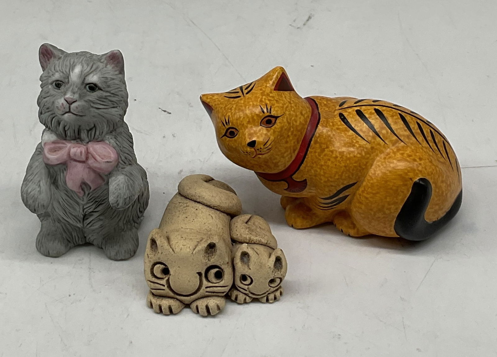 Lot 3 The Franklin Mint Cat Figurines 1980s: Lot of 3 The Franklin Mint ceramic cat figurines. Marked on underside, dated 1986. Features hand painted hand carved grey cat with textured features and pink bow detailed accents. Two hand carved beig