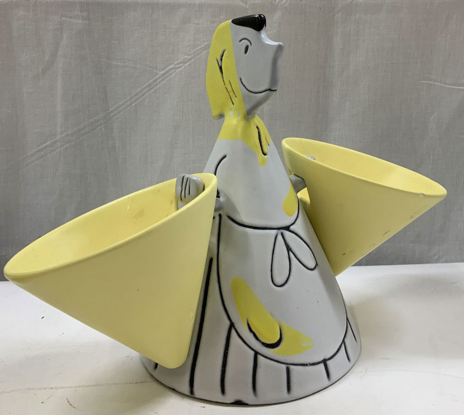 ANRI Ceramic Stylized Woman Condiment Holder: Ceramic figural condiment holder depicts a stylized woman with two large yellow side bowls. Hand-painted details. Yellow, white & black tones. Visible signature, reads, ANRI. Surface wear consistent t