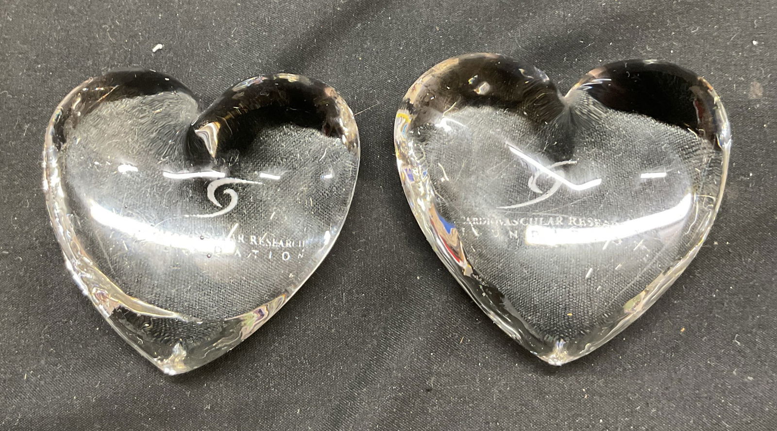 Pair Art Glass Heart Paperweights: Pair of art glass heart paperweights. Cardiovascular Research Foundation is etched into the surface with a swirl design. Measures approx 4 inches wide. Scratching observed and surface wear consistent