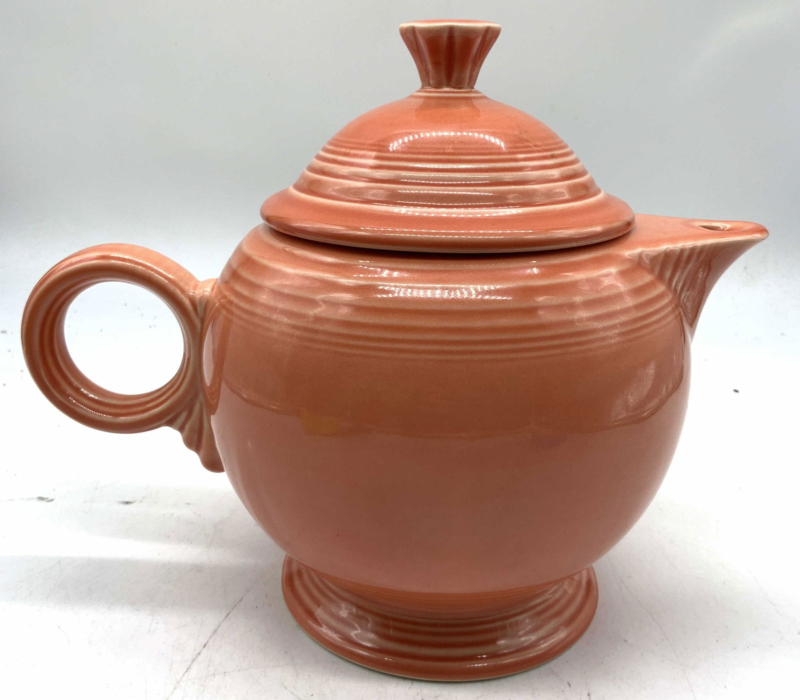 FIESTAWARE Peach Porcelain Teapot W Lid USA: Underside is inscribed FIESTA MADE IN USA. Teapot is porcelain. Piece is peach toned. Teapot includes lid and has circular form handle. Teapot measures approximately 7 inches tall 9 inches deep 5.5 in