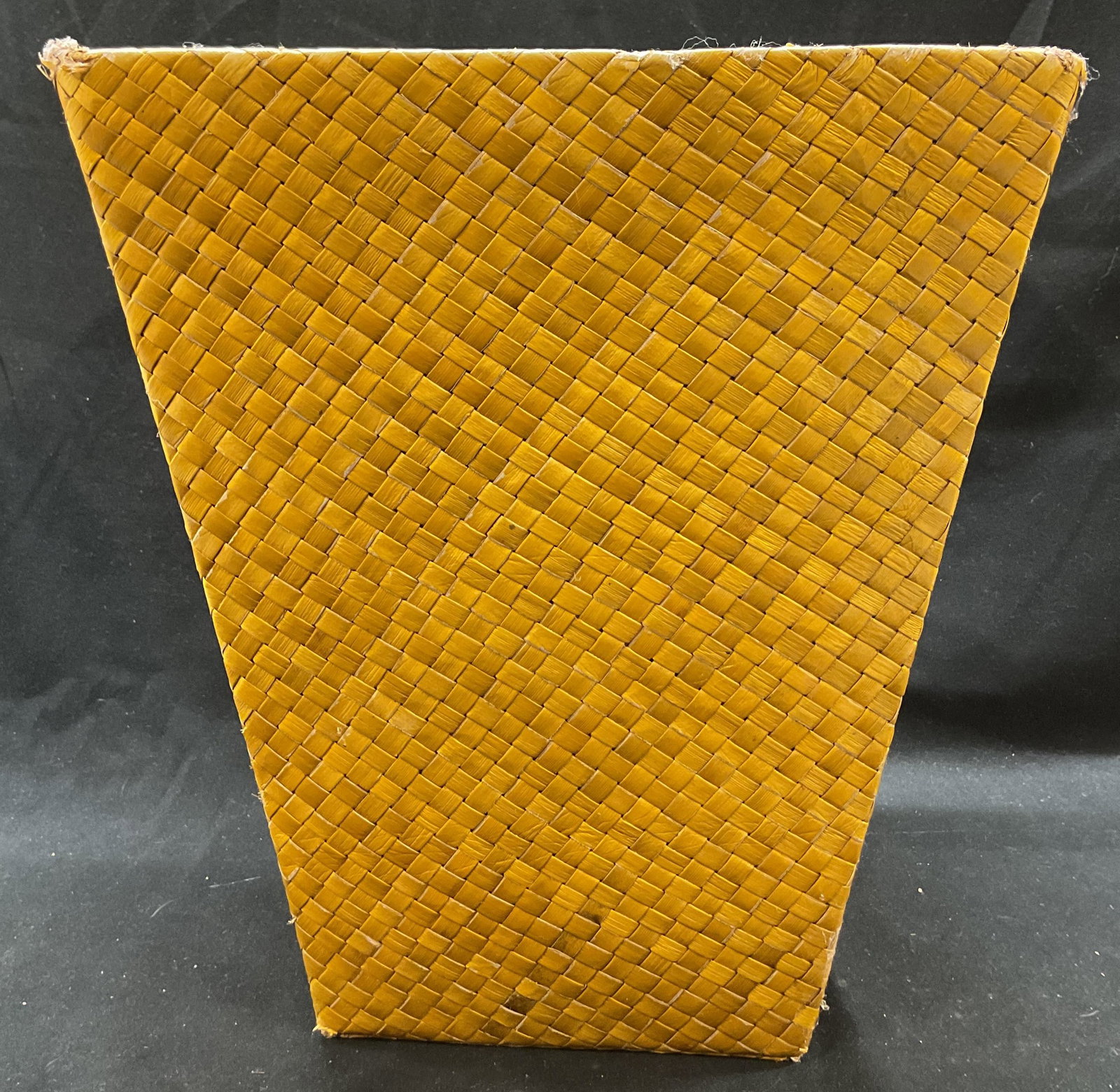 Rattan Style Woven Tan Waste Basket: Rattan style woven tan waste basket. Distinct rattan style basket weave pattern. Flared shape with wide rim and square base. Tan yellow color. Measures approx 10 x 6 x 12 inches. Slight fraying on rim