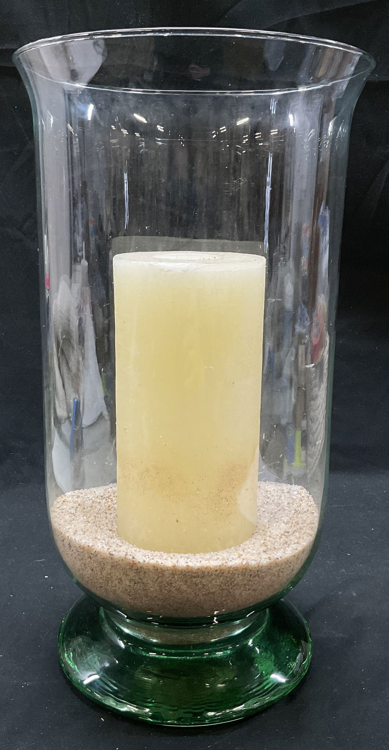 Vintage Large Glass Hurricane Candle Holder 16in: Vintage large glass hurricane candle holder. Pedestal base and flared rim. Green tinted base. Comes with off white pillar candle. Decorated with light colored sand as a base for the candle. Measures h