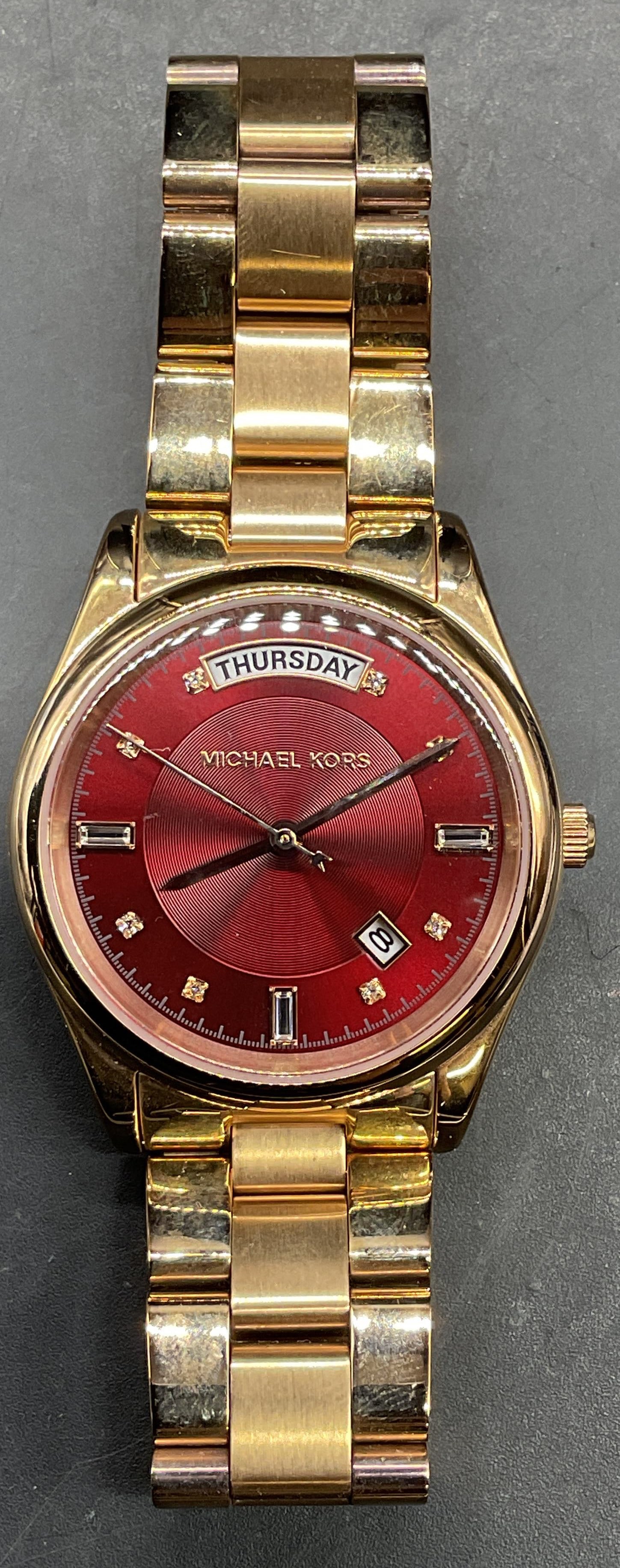 Michael Kors Gold Tone Red Wristwatch: Signed Michael Kors gold tone wristwatch with red dial. Dial measures approx 1.25 inches wide. Not tested. Some scratching. Jewelry, estate jewelry, costume jewelry, cocktail jewelry, fashion jewelry,