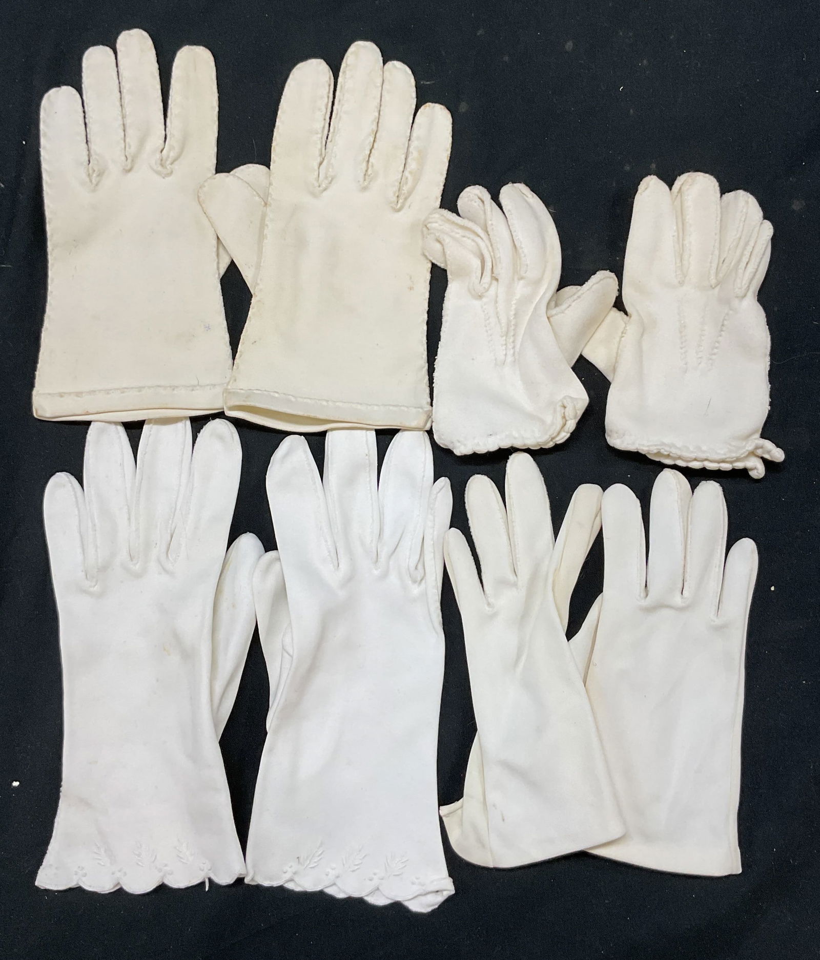 Lot 4 Vintage White Cotton Gloves: 4 pairs of vintage white gloves. Tags read illegible. All feel like cotton. Feature faux pearl accents, scalloped trim, and embroidered leaf motifs. Largest pair measure approx 3 inches wide 8 1/2 inc