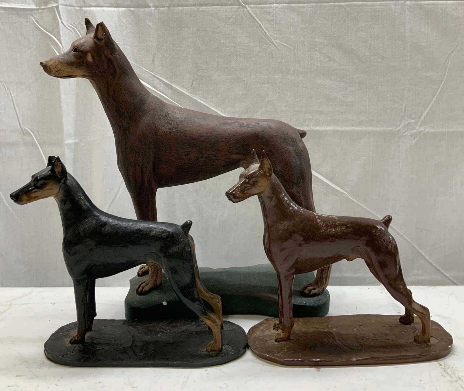 Lot 3 Standing Doberman Pinscher Statues: Lot includes, 1 black & 1 brown standing Doberman Pinscher statues. Lot also includes 1 brown Doberman ceramic statue. Dobermans are standing on an oval base. Assorted sizes. Surface wear consistent t