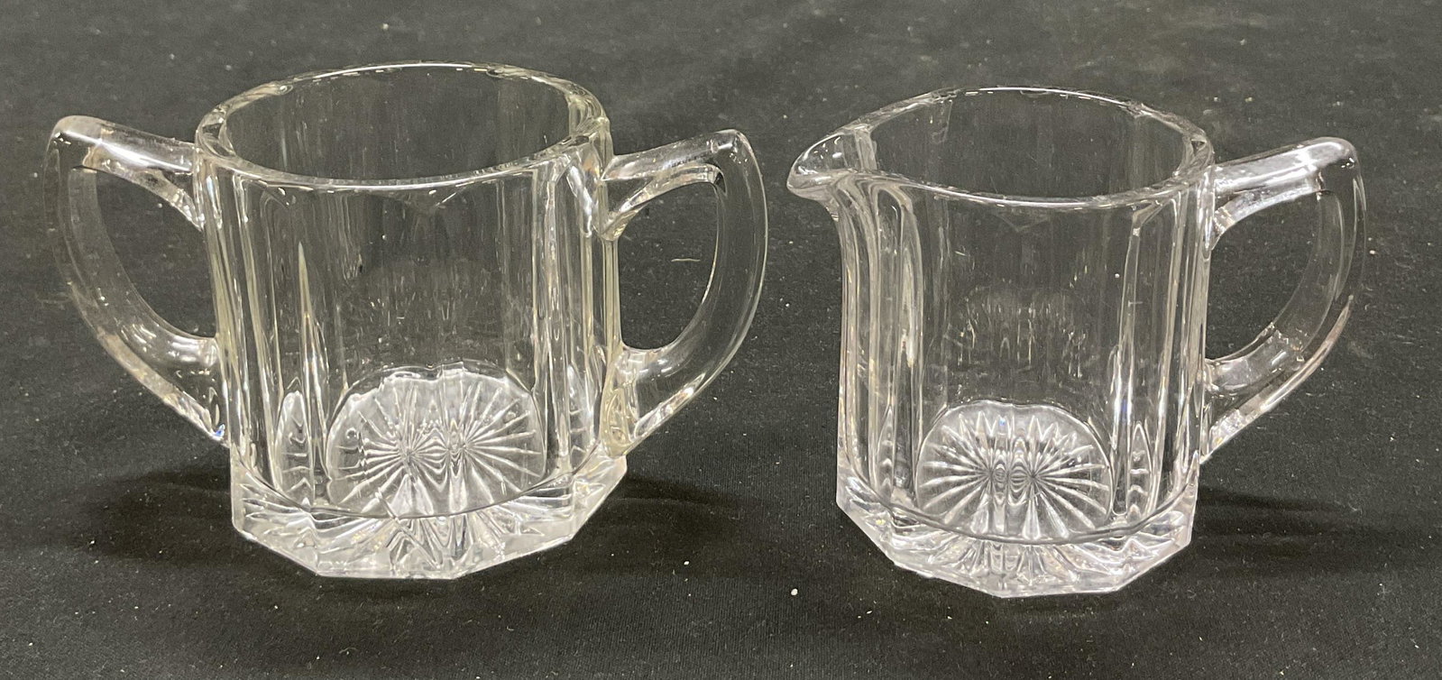 Set 2 Glass Sugar Bowl & Creamer: Set of 2 pieces. Includes glass sugar bowl and creamer. Faceted design and starburst design on underside. Angled handles. Largest piece measures ht approx 2 1/2 inches diam approx 4 inches. Some scrat