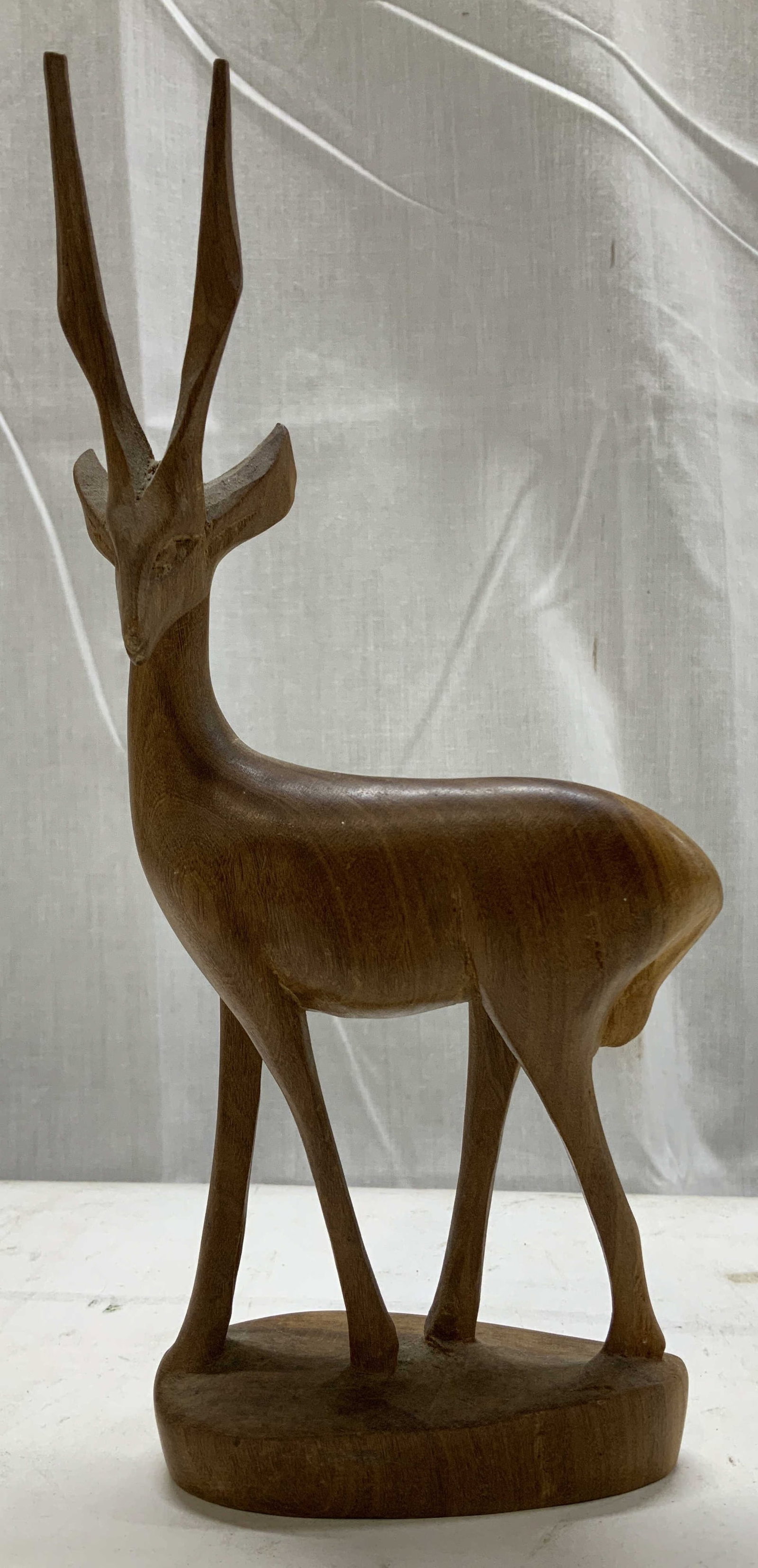 Hand Carved Wooden Antelope Figurine: Carved wooden antelope figurine, featuring a stylized design. Antelope is standing on a wooden base. Brown toned. Surface wear consistent to age, use & exposure. Measurements: length 3.5in x width 1.5