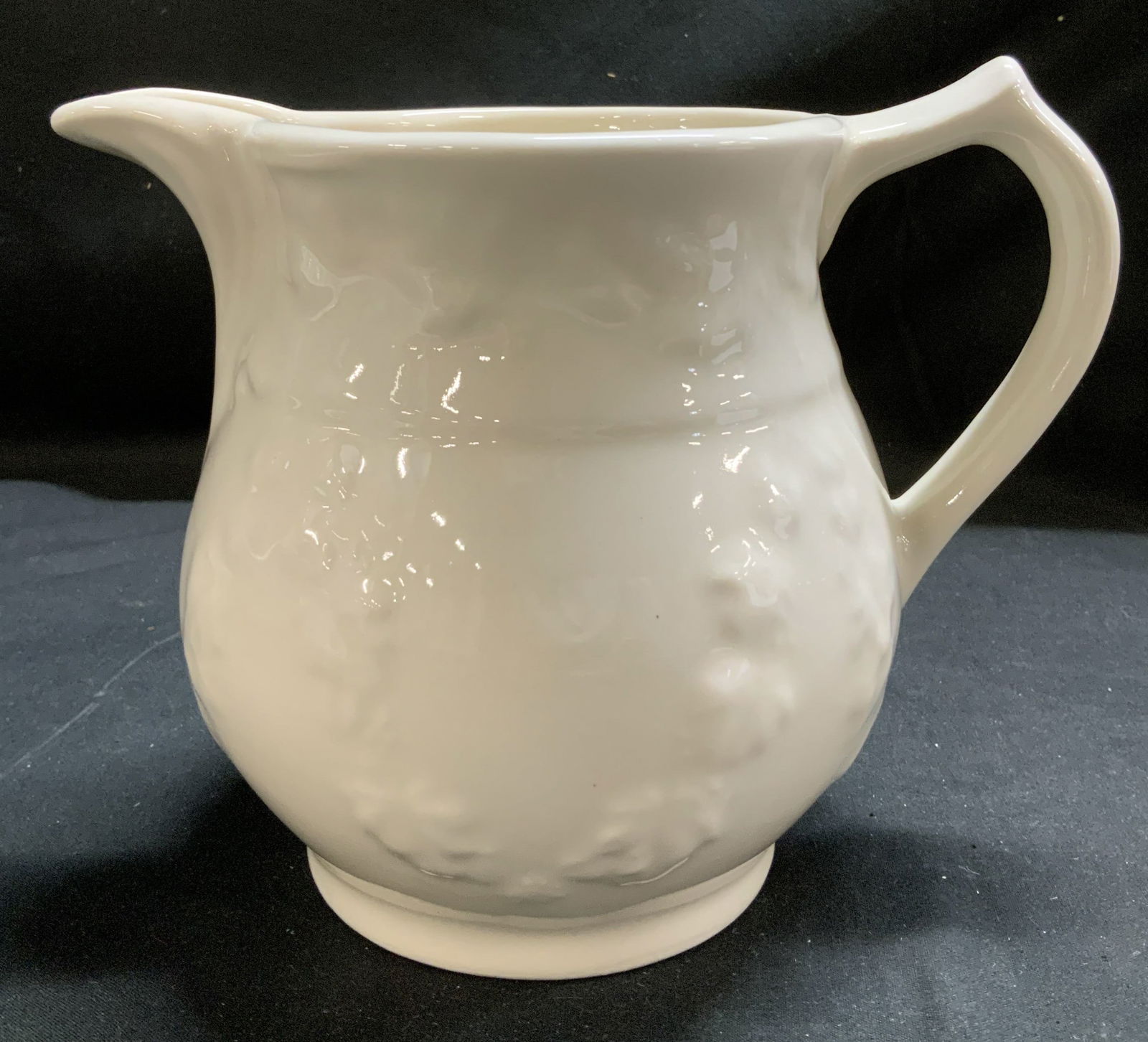 Hartstone White Stoneware Embossed Pitcher USA: White pitcher w an embossed floral pattern on body. Glossy finish. Appears to be possible stoneware material. Signed & marked on underside. Reads, HARTSTONE USA. Surface wear consistent to age, use &