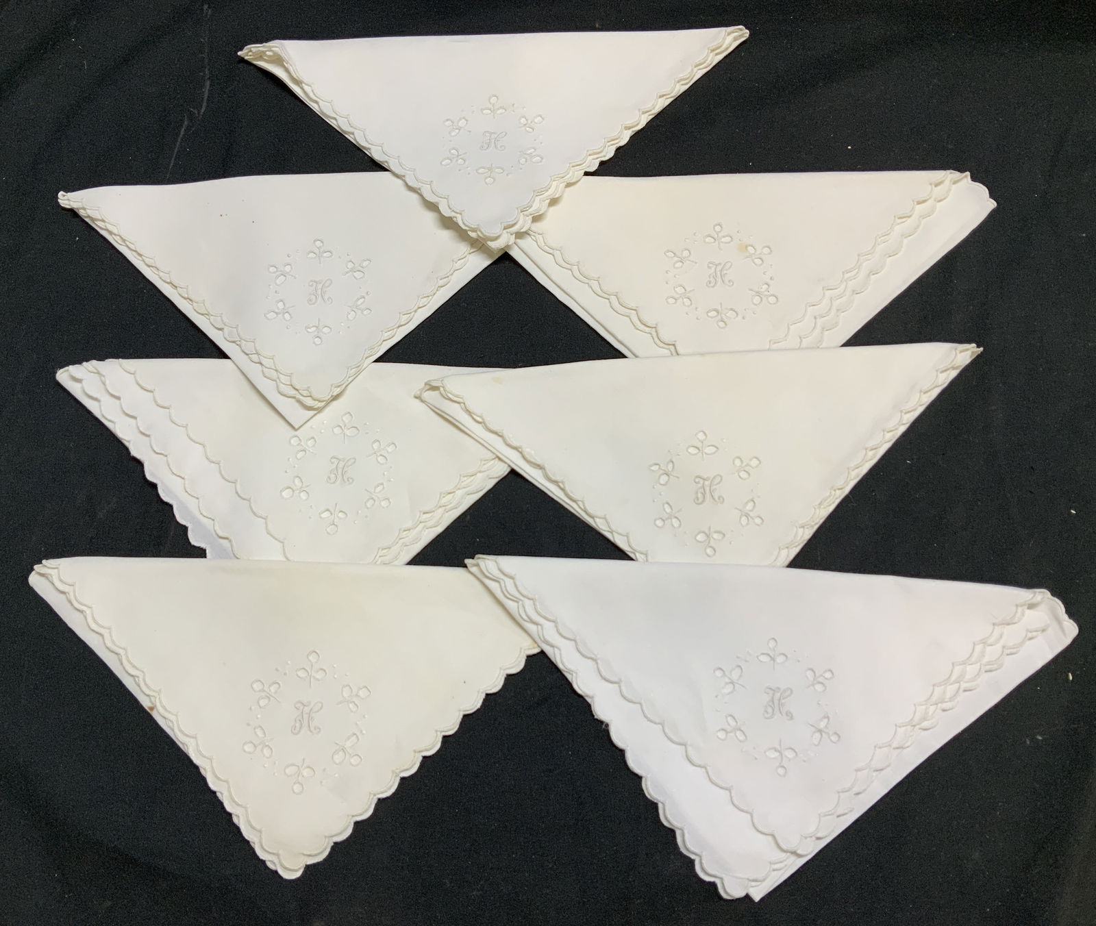 Set 7 Vtg White Embroidered Linen Napkins: Lot includes, set 7 of white napkins featuring a scalloped edge and a hand-embroidered floral cutwork. Small embroidered H. Appears to be possible linen. Surface wear consistent to age, use & exposure