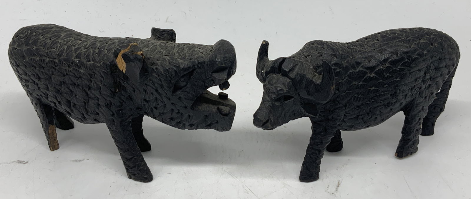 Lot 2 Hand Carved Wooden Buffalo & Hippo Figs: Lot includes, 2 hand-carved wood figurines depicting water Buffalo & hippopotamus. Black toned with intricate detailing. Surface wear consistent to age, use & exposure. Measurements: length 5.3in x wi
