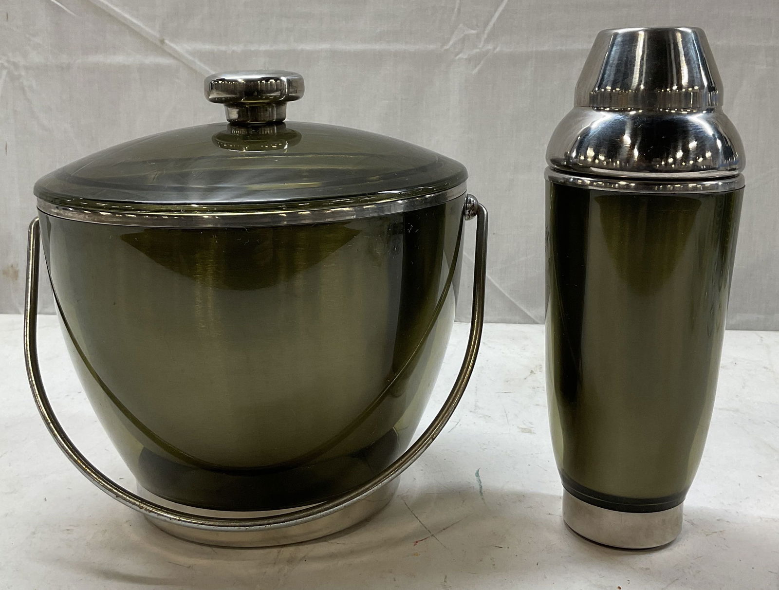 Set 2 Stainless Steel Ice Bucket & Cocktail Shaker: Set of 2 items. Includes green stainless steel ice bucket with lid and handle. Green stainless steel cocktail shaker with lid. Largest piece measures ht approx 9 inches diam approx 8 1/2 inches. Scrat