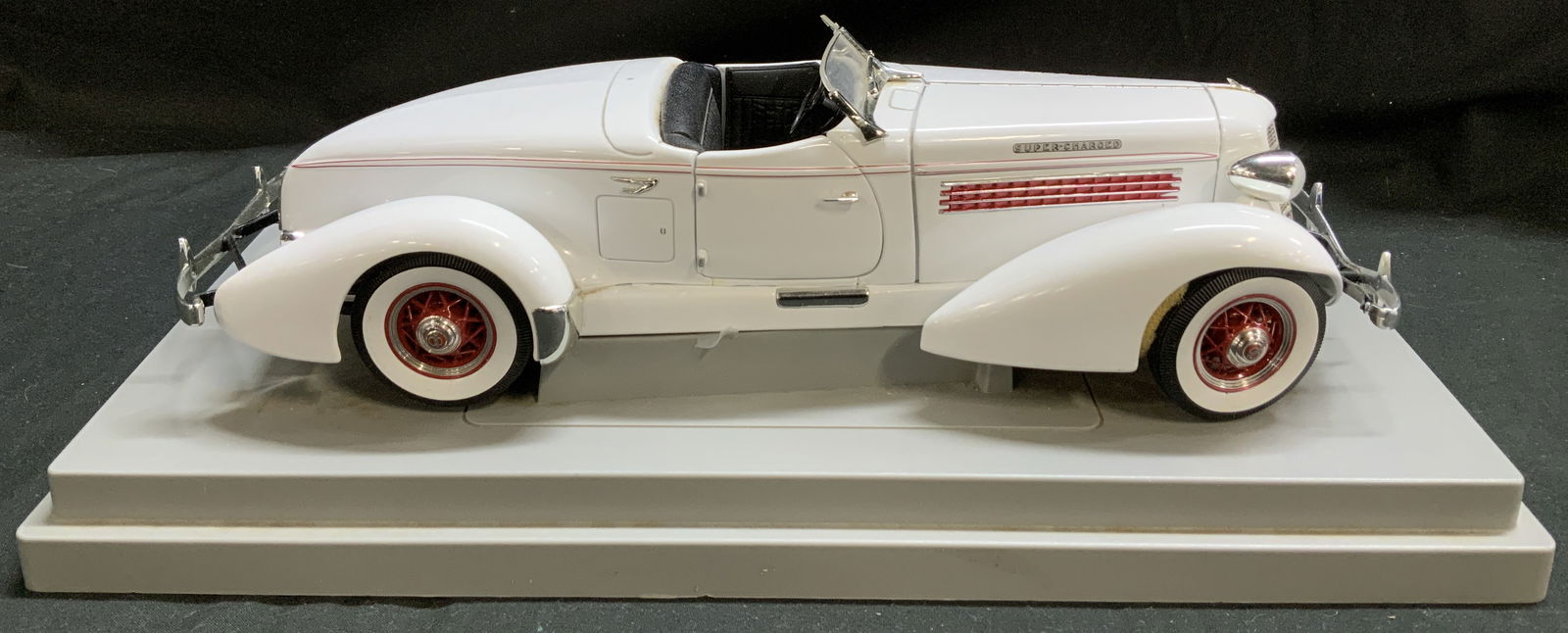 1935 Auburn 851 Boattail Speedster Model Replica: Die-cast model replica of a 1935 Auburn 851 Boattail Speedster. Car features a white exterior with red accents on wheels. Interior is black toned. Hood of car opens & reveals engine. Surface wear cons