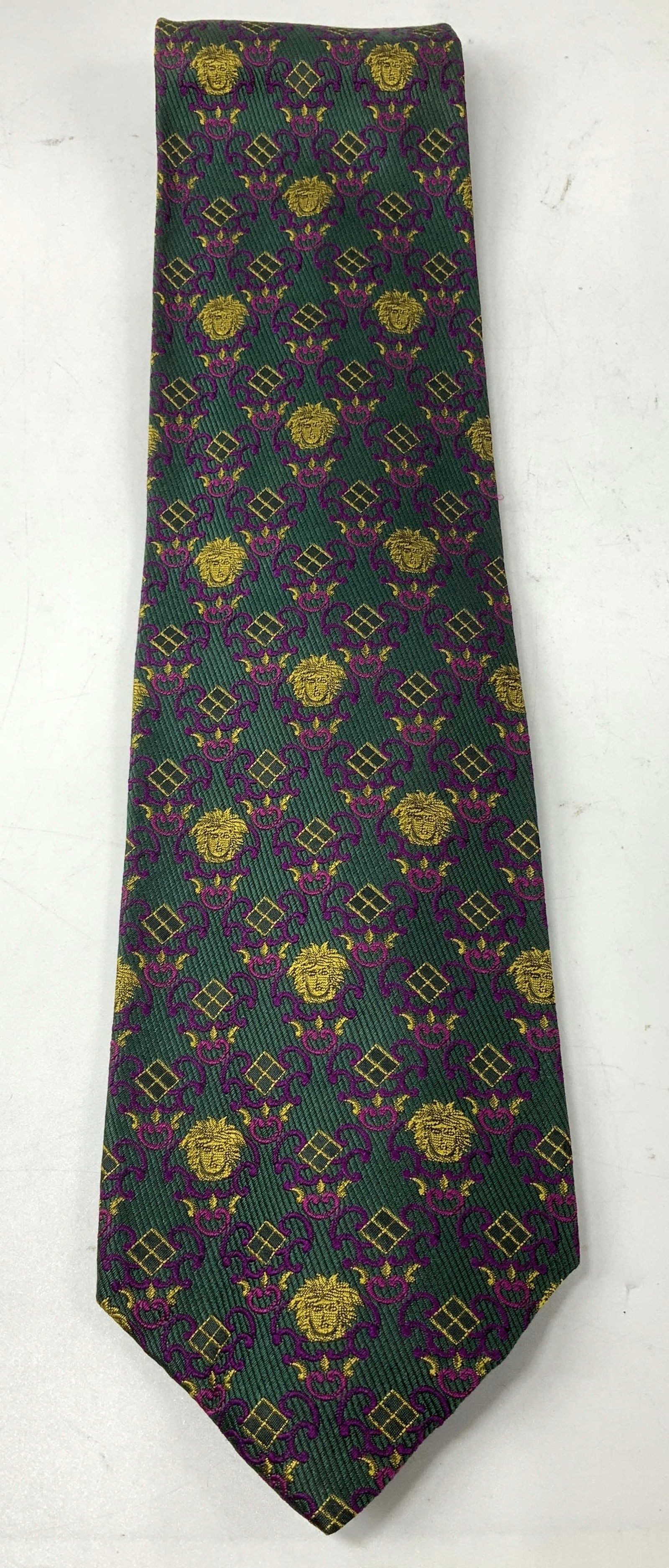 Gianni Versace Stylized Heads Silk Necktie ITALY: Necktie is 100% silk & features shades of green, purple & yellow. Repeating pattern of stylized head motifs. Signed & marked. Reads, GIANNI VERSACE. MADE IN ITALY. Surface wear consistent to age, use