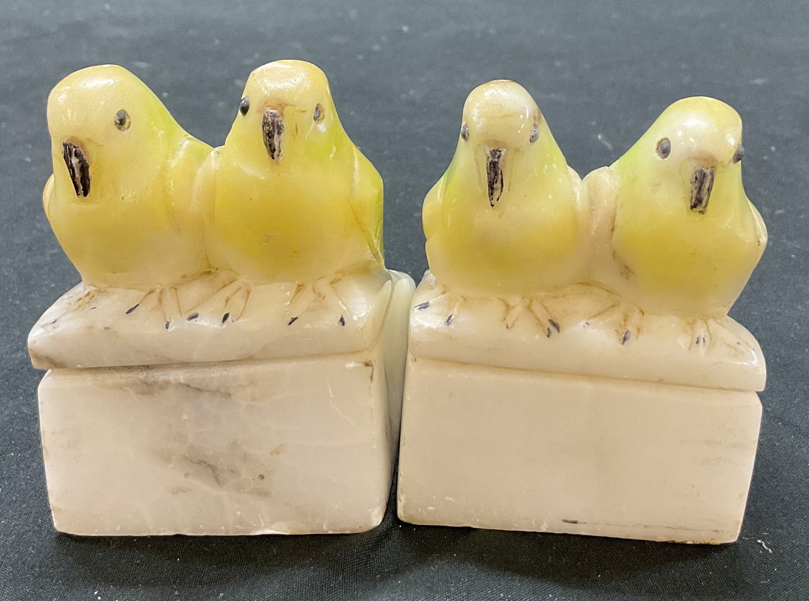Pair Carved Stone Birds Sitting Bookends: Pair of carved stone bookends. Depicts two birds sitting on a stone base. Side by side. Hand carved detailing on bird figures. Colors include white, black, and yellow. Some marks on underside. Measure