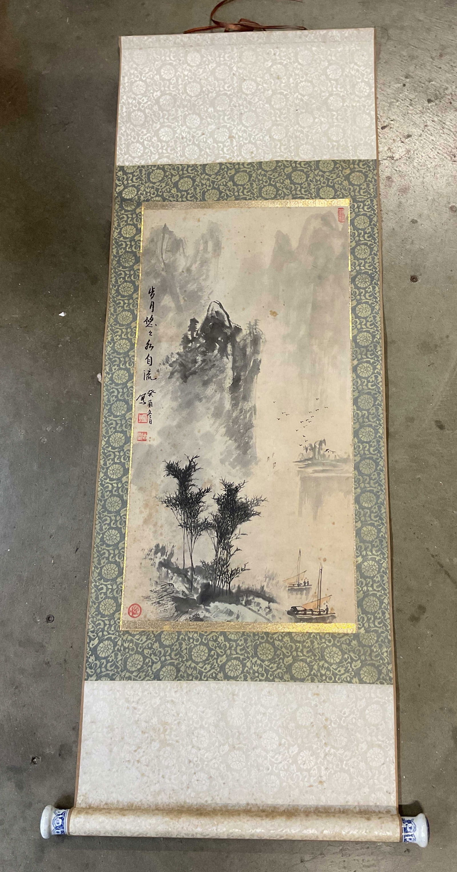 Vintage Hand Painted Chinese Scroll 48in: Vintage hand painted Chinese scroll. Hand painted ink on paper. Decorative floral motif fabric border surrounding central image. Image depicts a landscape with trees, figures, birds, water, mountains,