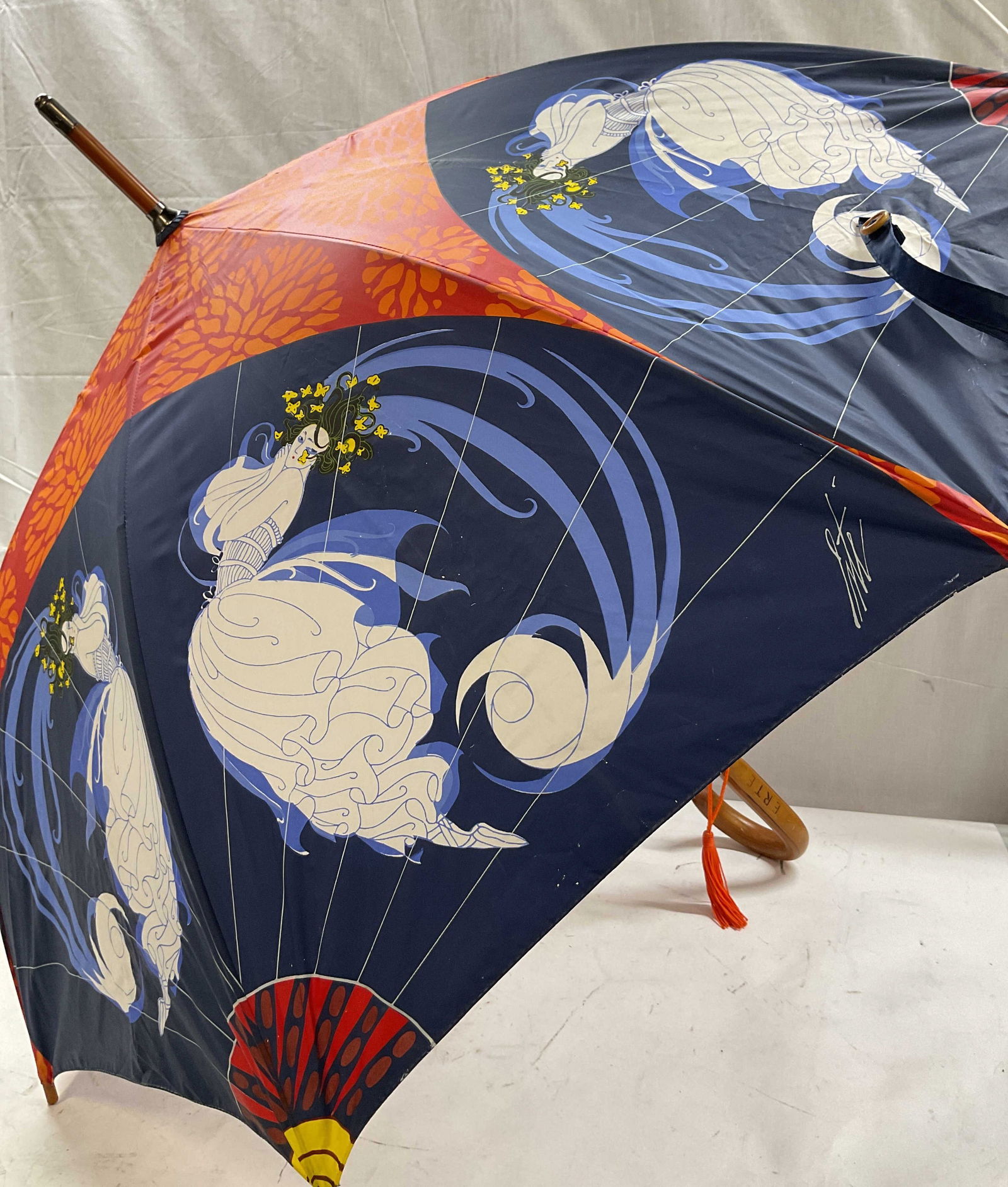 ERTE Wood Curved Handle Figural Umbrella: Vintage ERTE wood curved handle figural pattern umbrella. Wood curved handle with signed ERTE carved. Nylon material. Mainly blue, white, orange, red, and yellow. Depicts woman figure with details and