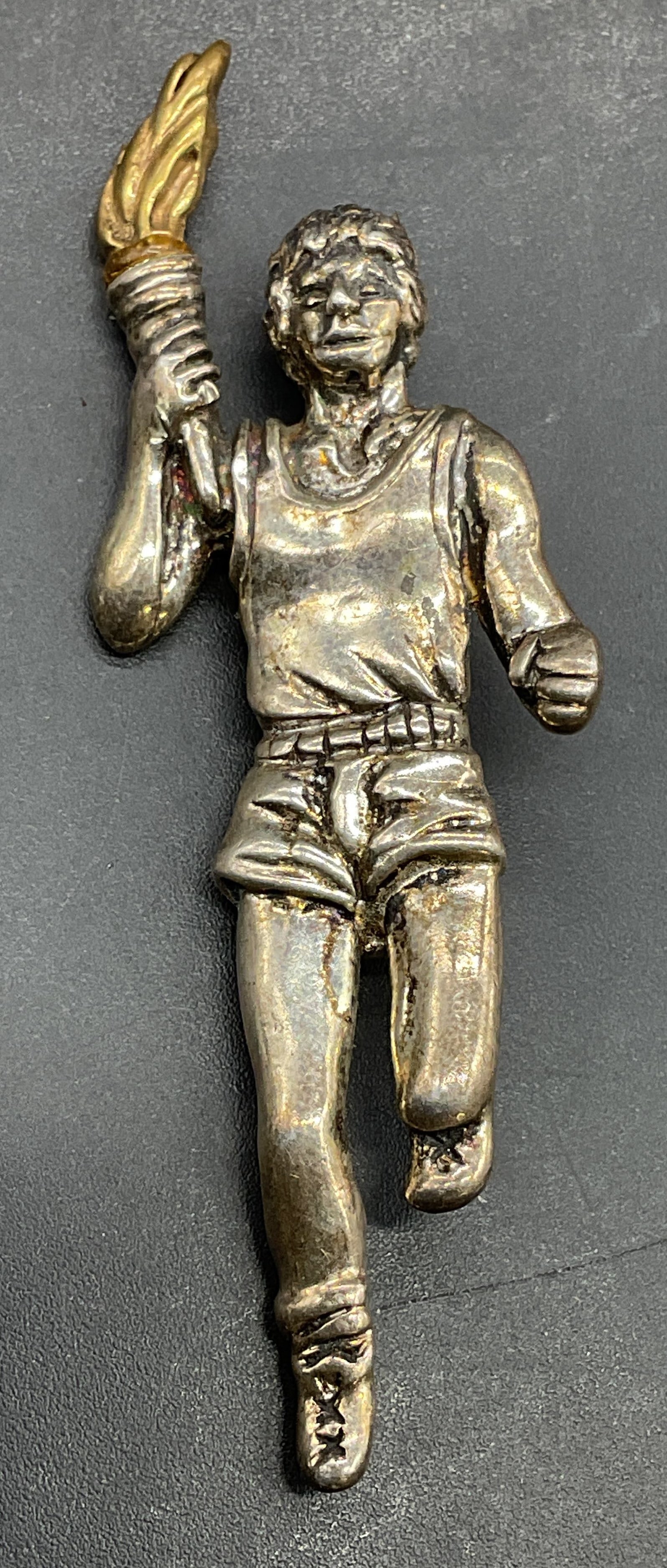 Signed Sterling Silver Olympic Runner Brooch: Signed Sterling silver and gold tone Olympic runner holding torch motif brooch. Measures approx 2.5 x 7/8 inches. Total weight 9.9 grams. Marked sterling., additional marks illegible. Some scratching.
