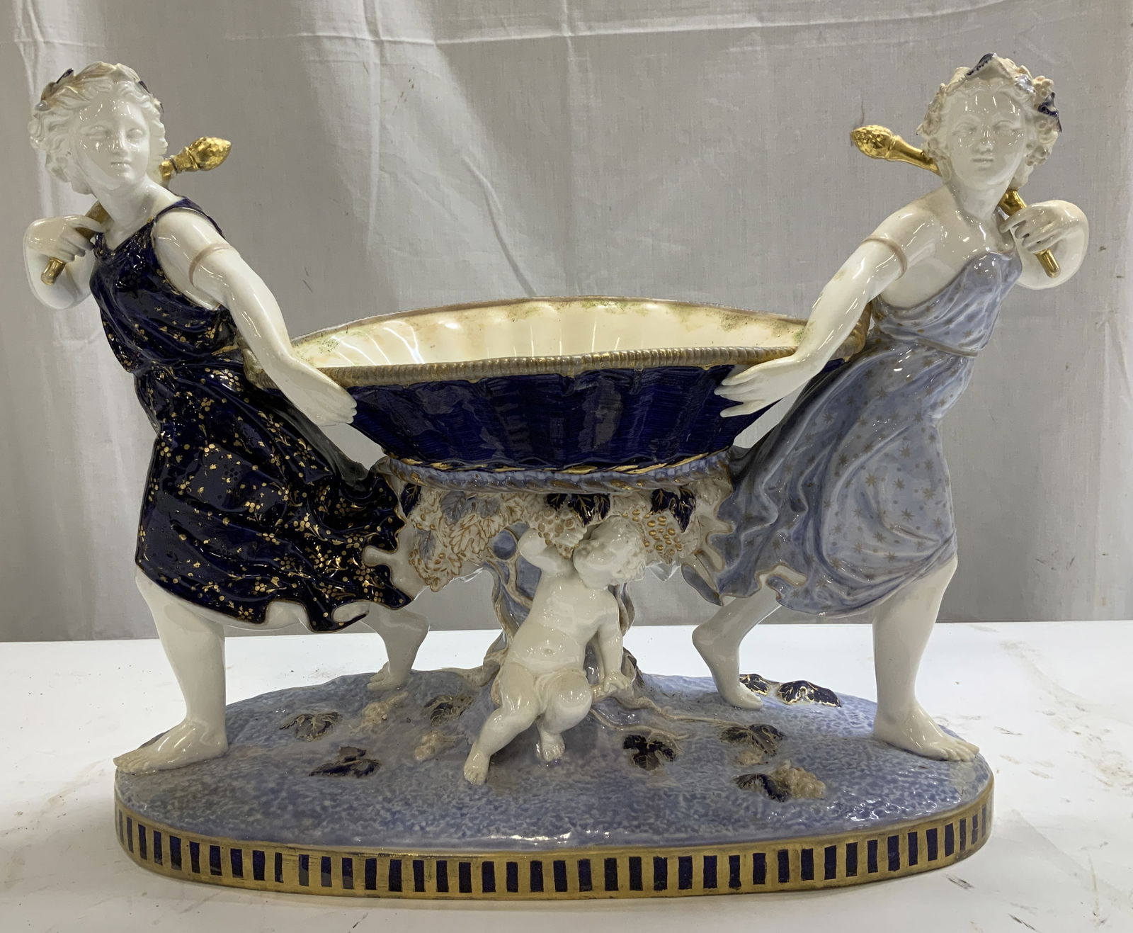 Vtg Classical Figs W Cherub Centerpiece Compote: Centerpiece compote is ceramic & depicts 2 classical female figures wearing long wavy dresses. They each appear to be holding a staff & are supporting a center bowl. Underside of bowl has a cherub fig