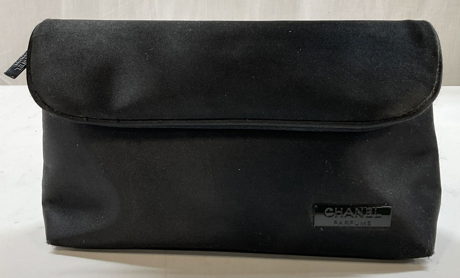Chanel Black Makeup Bag: Chanel black makeup bag. Feels like silk. Features fold over flap and zipper. Lining printed with Chanel logo. Measures approx 5 1/2 x 9 1/2 inches. Surface wear consistent with exposure. Property of