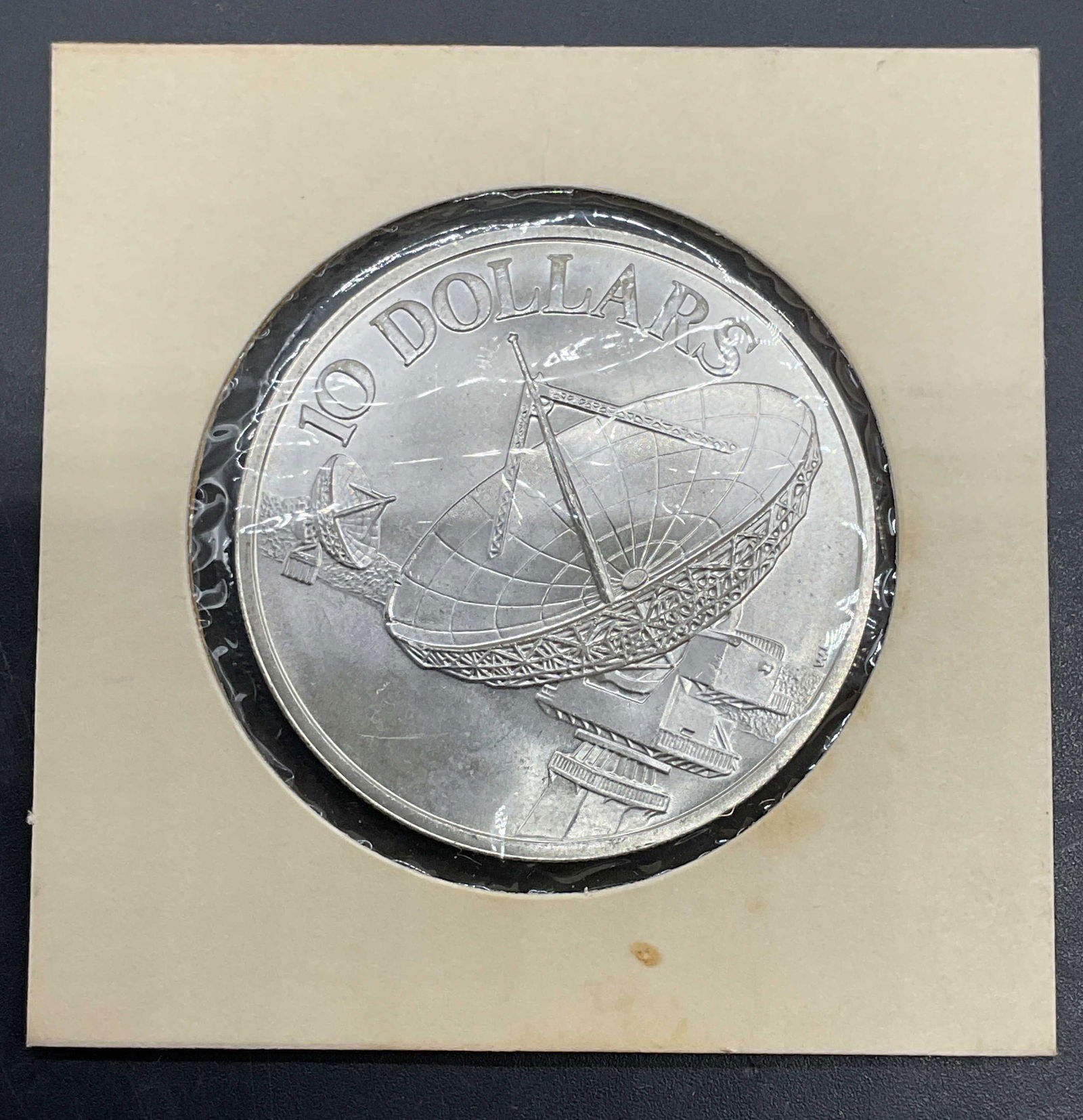 1979 Singapore 10 Dollar Coin, 500 Silver: 1979 Singapore 10 dollar coin. 500 silver. Reverse feature satellite, obverse features coat of arms. Measures approx 1.5 inches wide. Held in protective cover, not examined out of cover. Total weight
