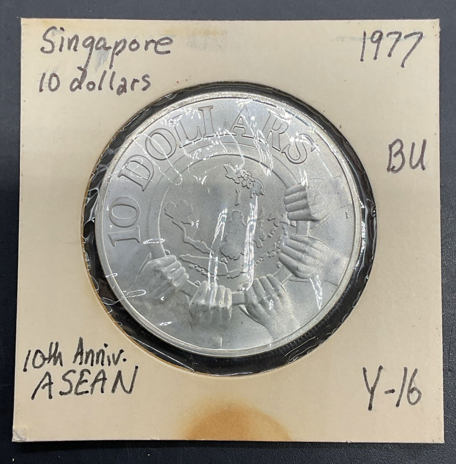 1977 Singapore ASEAN Anniversary Coin 500 Silver: 1977 Singapore 10 dollar coin commemorating the ASEAN 10th anniversary. Reverse features hands around aerial view of Singapore, obverse features coat of arms. Measures approx 1.5 inches wide. Held in