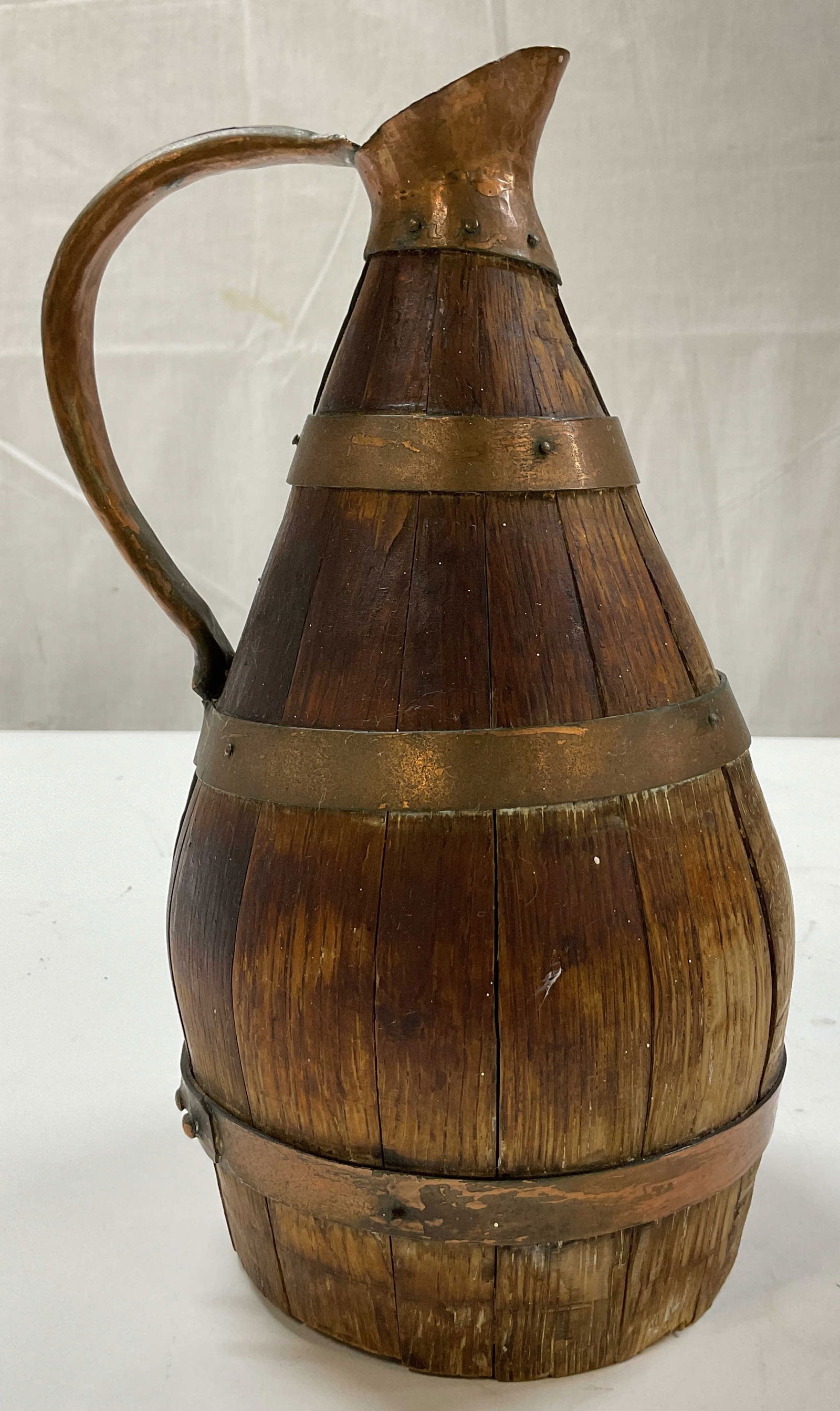 Vintage Wood Copper Toned Wine Pitcher: Vintage wood copper toned wine pitcher. Constructed from wood in a barrel style shape with copper toned bands. Curved copper toned handle and spout. Bulbous body. Measures ht approx 11 inches base dia