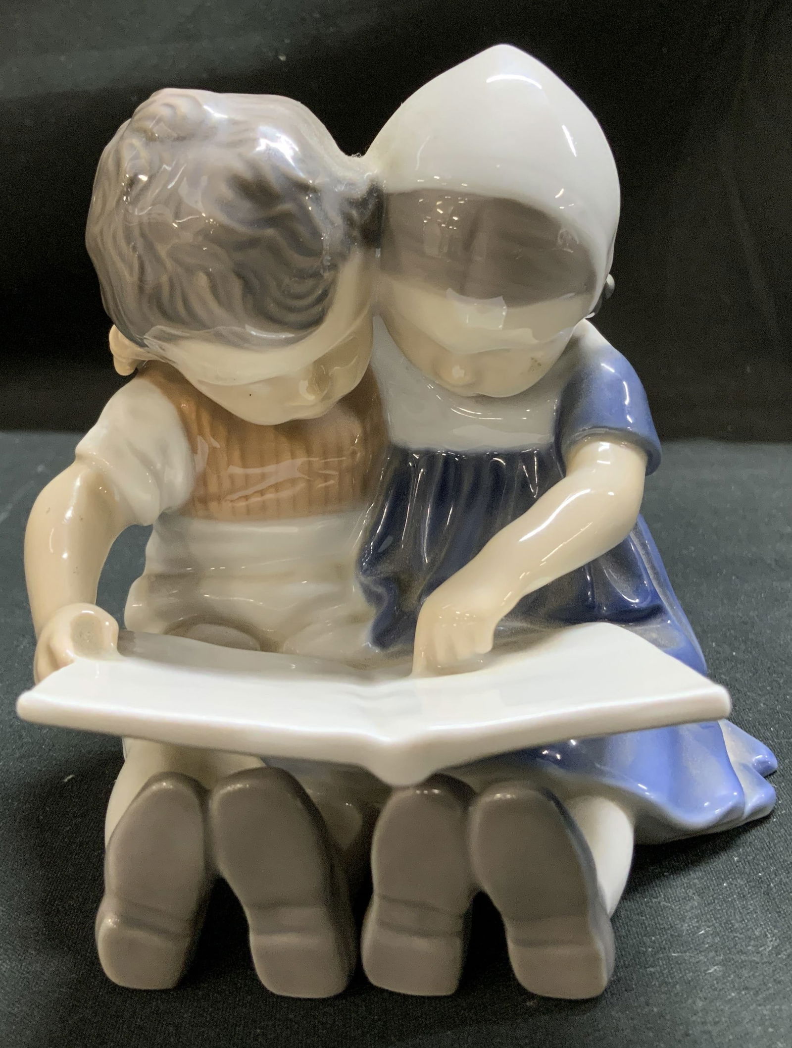 Bing & Grondahl Children Reading Porc Fig DENMARK: Porcelain figurine depicting a young boy & girl seated together reading a book. Glossy finish. Signed & marked on underside. Reads, DANMARK B & G. MADE IN DENMARK. 1567. Surface wear consistent to age