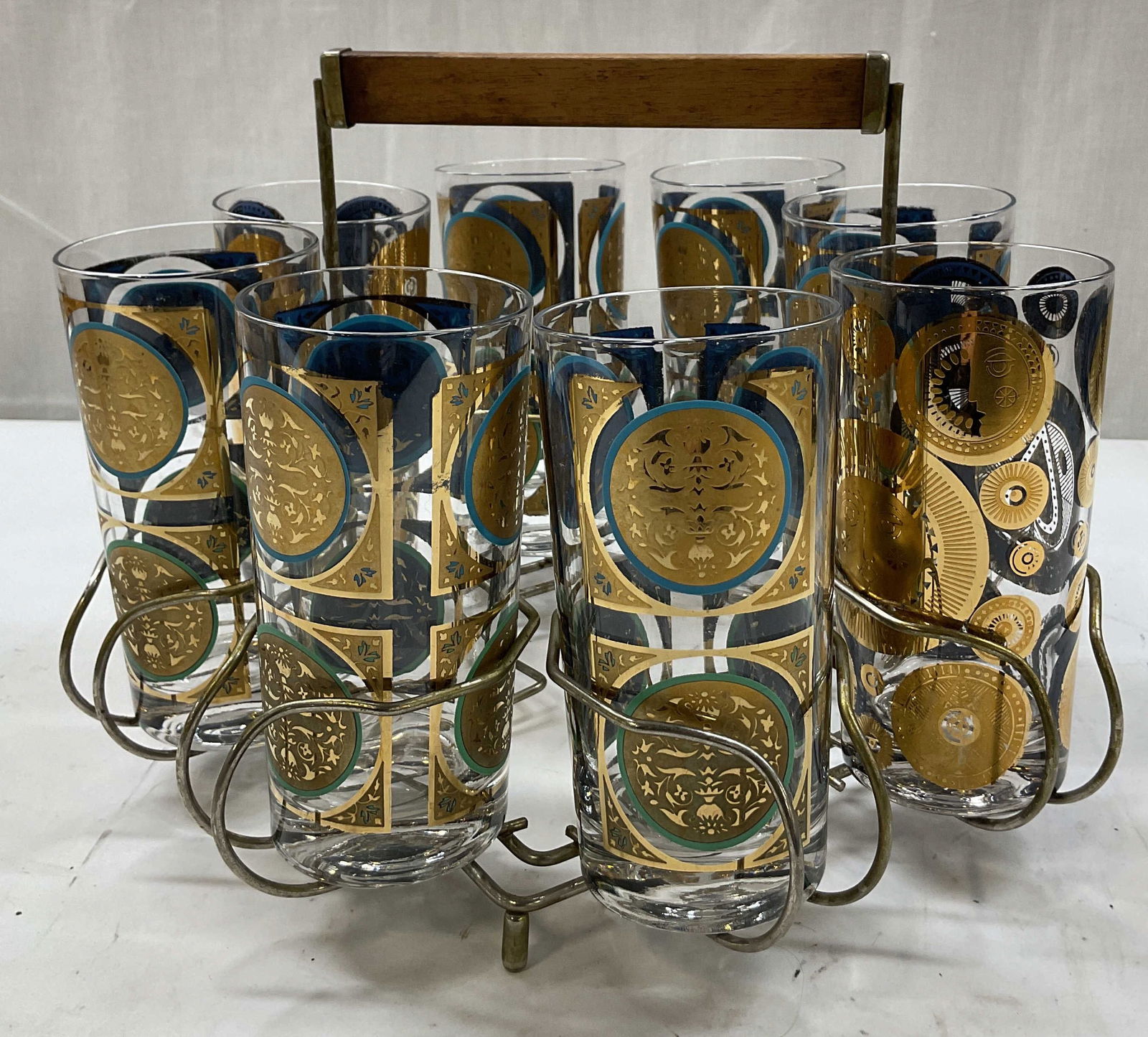 Set 8 SGND Georges Briard Highball Glasses W Caddy: Set of 8 Georges Briard highball glasses. Comes with wireframe caddy. Signed on side, reads Georges Briard. Cylinder shaped glasses. Features gilt decorated designs. Medallion patterns including faces