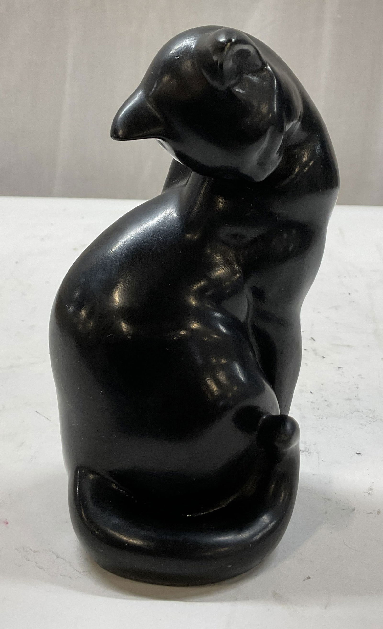 Vintage Black Ceramic Cat Figurine USA: Vintage black ceramic cat figurine. Sticker adhered to underside reads made in Vermont. Seated pose head looking down with tail curled around its body. Detailed textures and features. Measures approx
