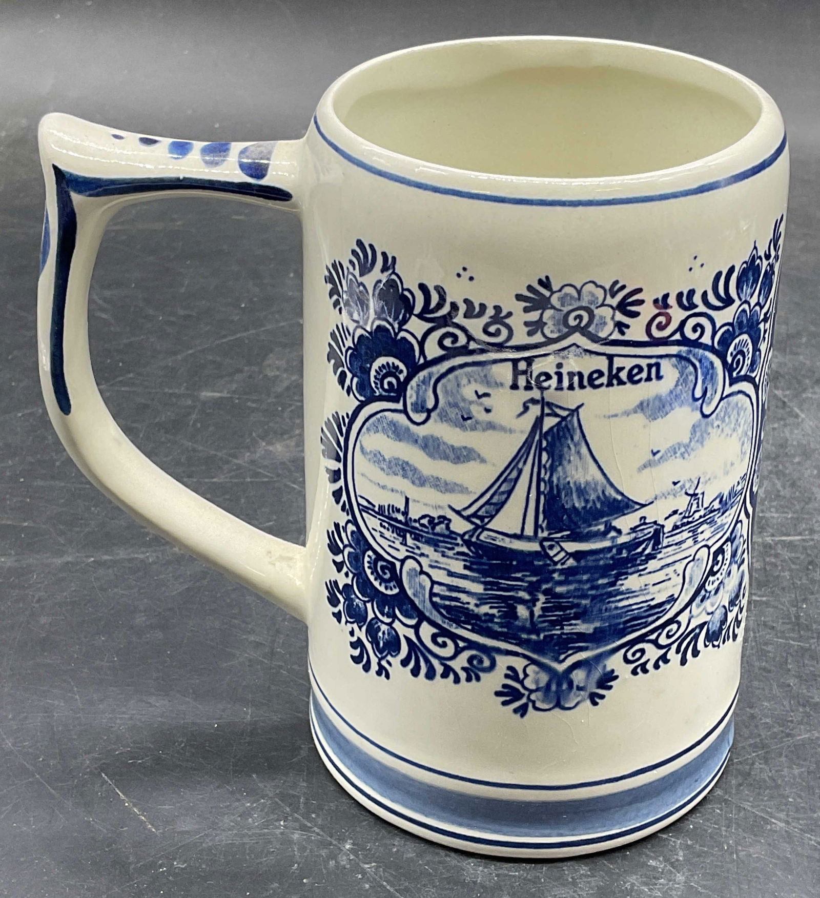 GKB Heineken Delft Blue Ceramic Beer Stein Holland: Signed GKB delft blue ceramic Heineken beer stein. Dutch scenes, boat on water and windmill, hand screened. Signed on underside. Made in Holland. Measures approx 5 x 3.5 x 5.5 inches. Wear