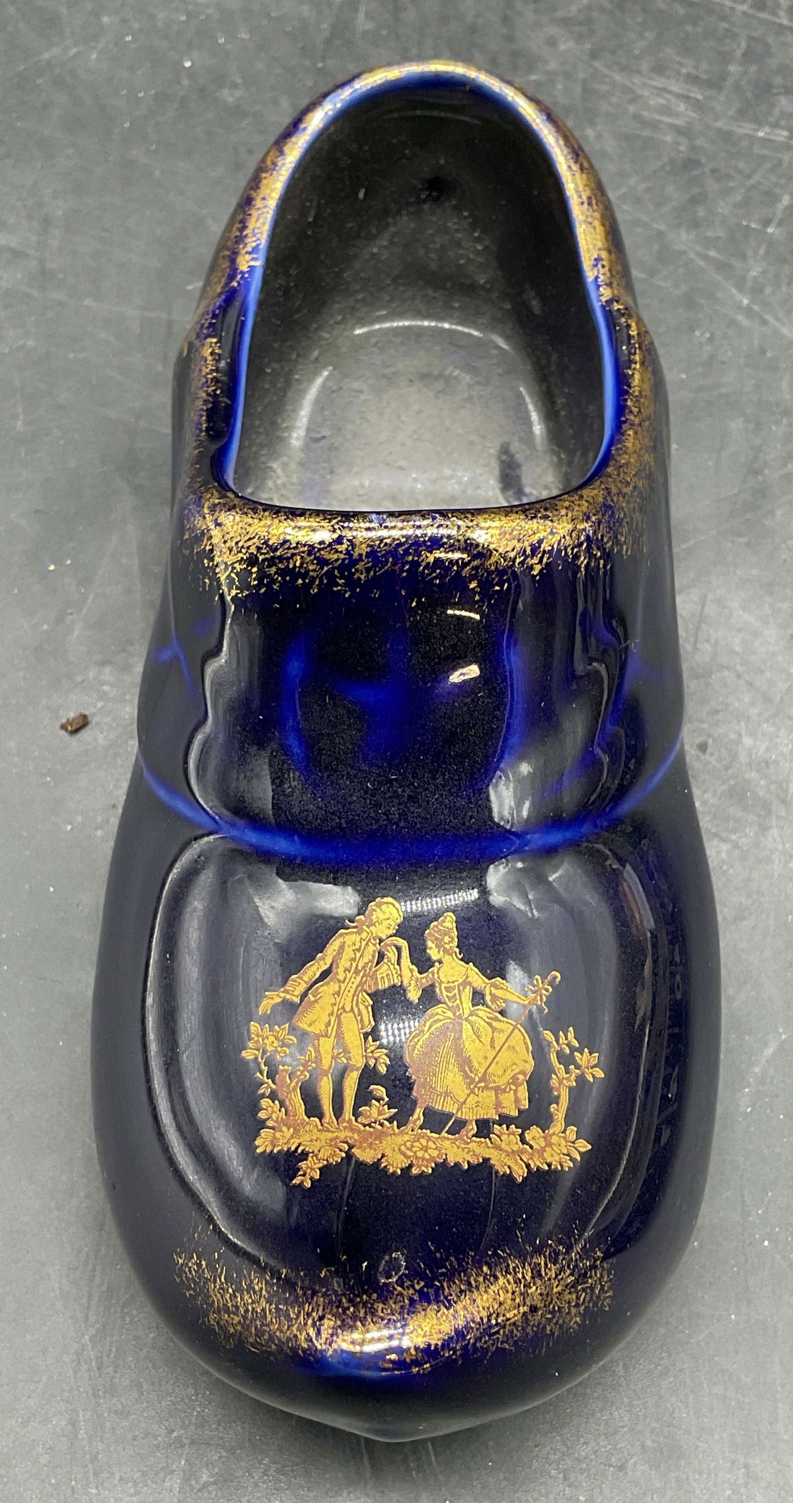 Le Trefle Limoges Porcelain Dutch Shoe, France: Le Trefle Limoges porcelain Dutch shoe figurine. Cobalt blue with gilt decoration and couple motif. Signed. Made in France. Measures approx 5.5 x 2.25 x 2.25 inches. Some wear consistent with