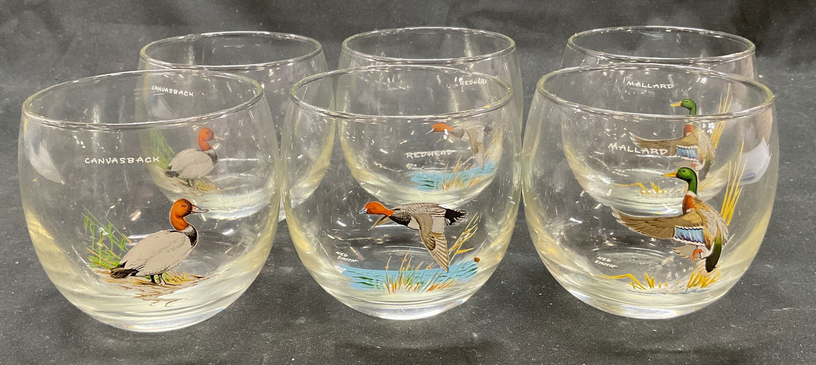 Set 6 Ned Smith Duck Wine Glasses: Set of 6 Ned Smith figural duck wine glasses. Signed Ned Smith with different species of duck names such as Mallard, Redhead, and Canvasback. Depicting images of these ducks in colors green, blue, red