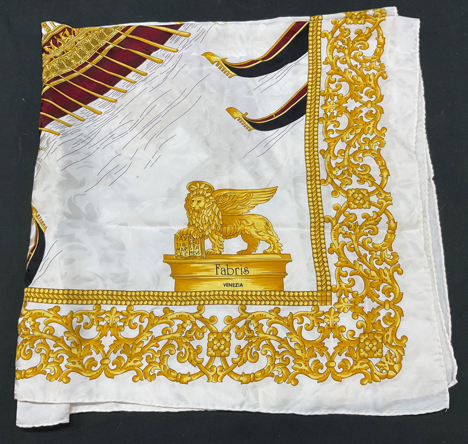 Fabris Venezia White Silk Scarf Italy: Fabris Venezia white silk scarf. Made in Italy. Silk material. White background with yellow ornate scroll border. Reads Fabris Venezia on a lion statue. More animal figurals and boat motifs.