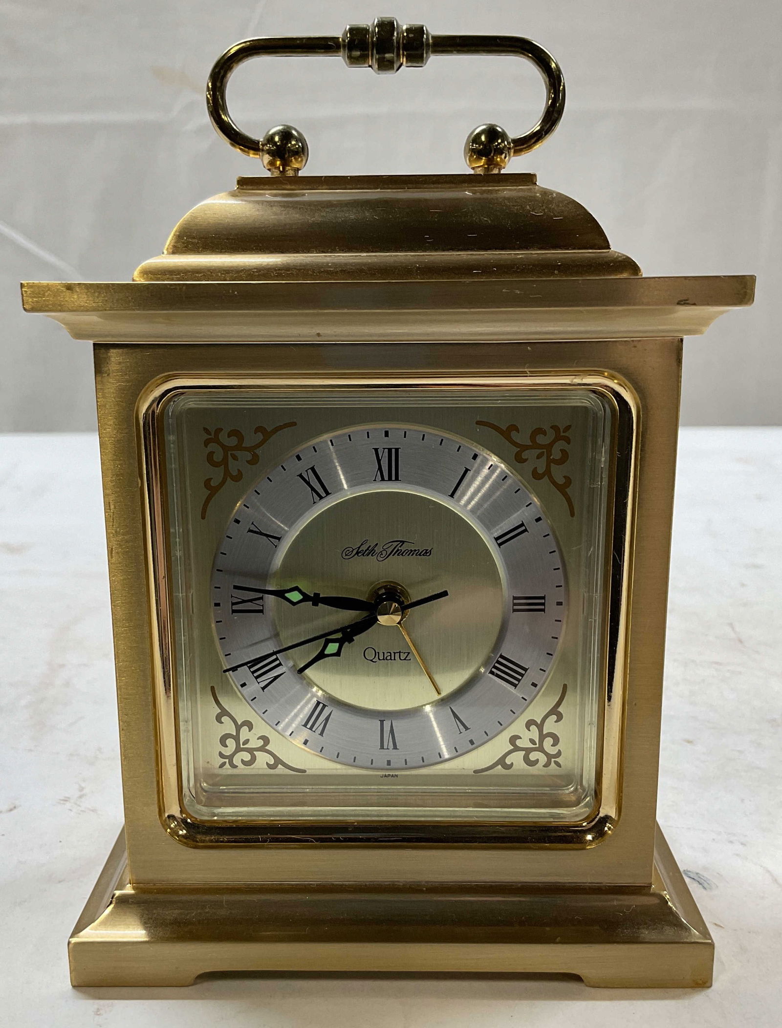 Seth Thomas Rapture Brass Quartz Alarm Clock: Seth Thomas rapture brass quartz alarm clock. Crafted from solid brass. Carriage style with handle at the top. Includes Roman numerals and ornate gold toned scrollwork in each corner. Center is marked