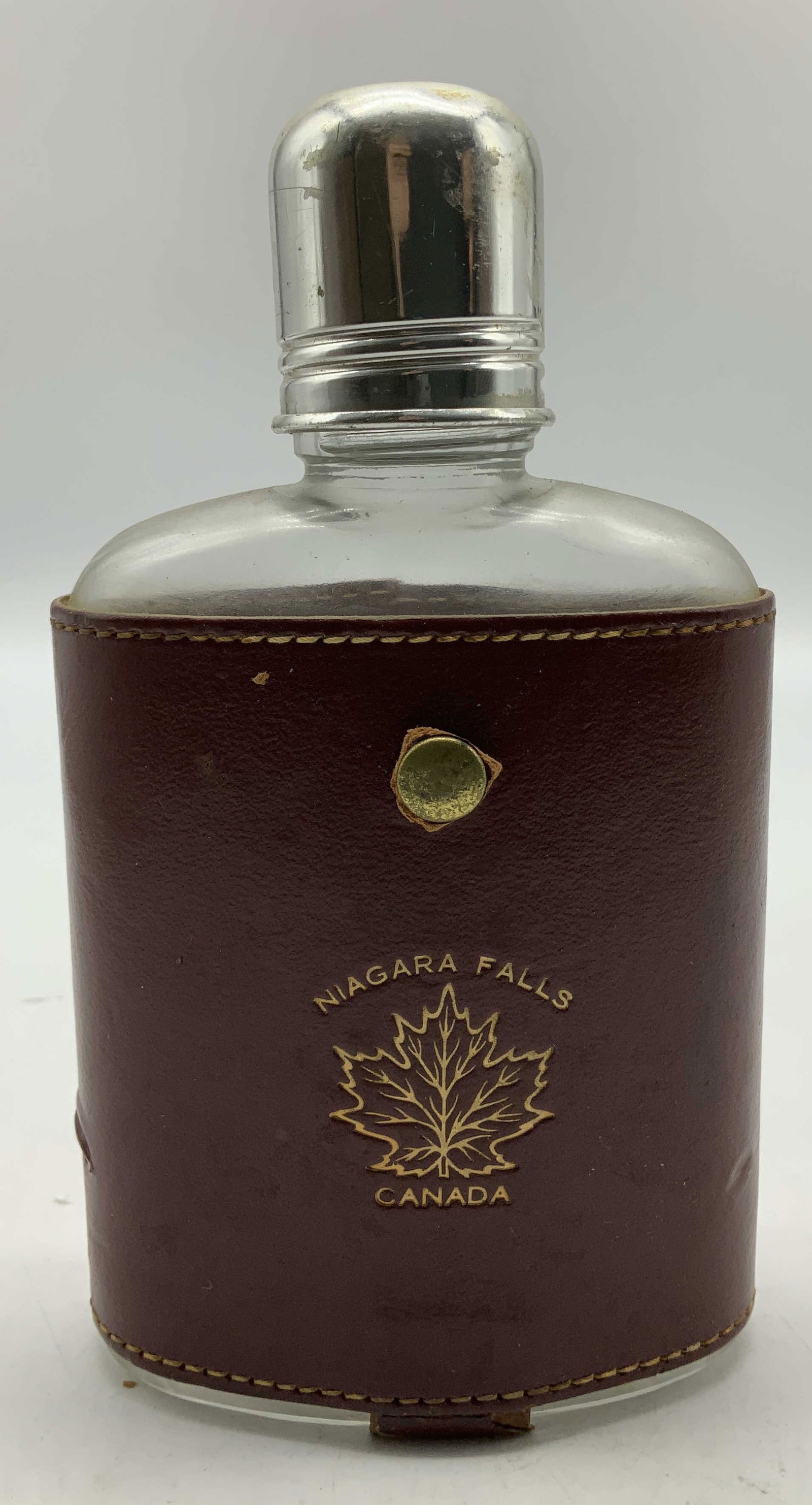 Vntg Leather Wrapped Niagara Falls Canada Flask: Vintage glass flask with a maroon leather wrap featuring Niagara Falls Canada text & a maple leaf emblem. Silver toned top. Property of Upper East Side French & screen actors Estate, Manhattan.