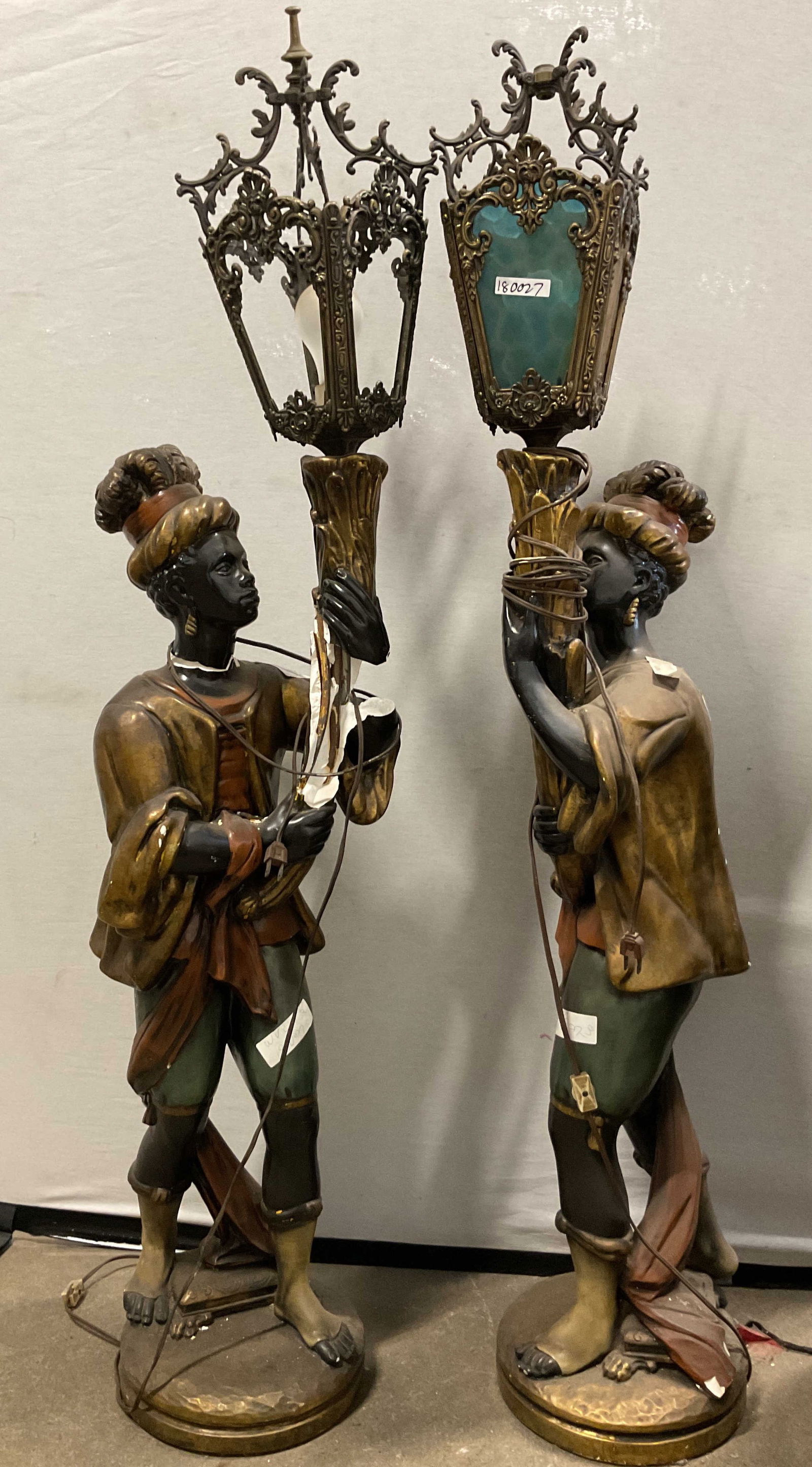 Pair Vintage Composite Figural Lamps 50in: Pair of vintage composite figural lamps. Two figures hold up the lamps like torches. Composite material and metal. Standing on circular bases. Lamps have panels of glass. Ornate designs and