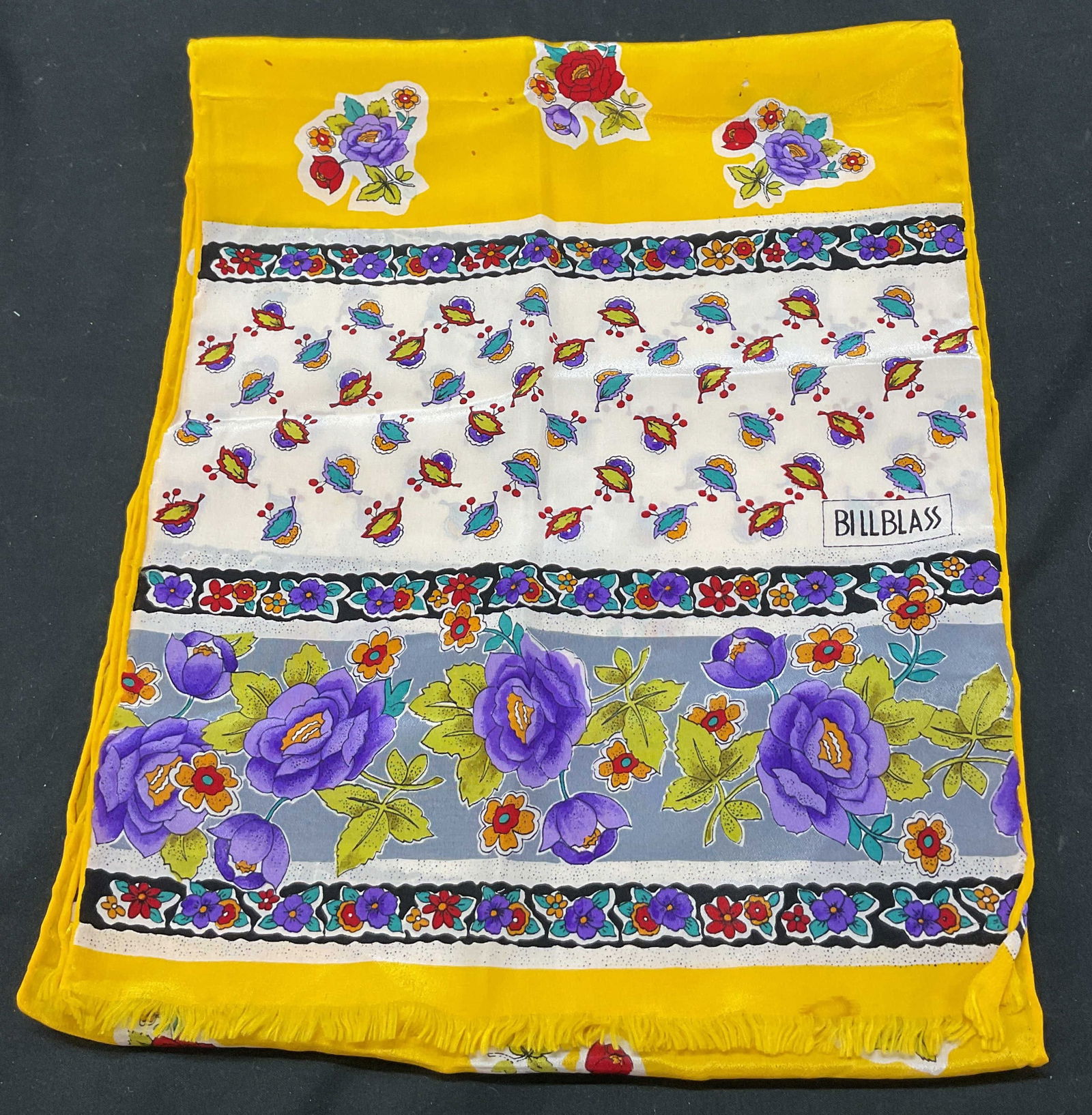 Billblass Yellow Fringed Floral Silk Scarf: Billblass yellow fringed floral silk scarf. Feels like silk. Yellow fringed trim. Yellow background. Floral motif pattern. Colors include red, purple, green, blue, and more. Measures approx 11 x