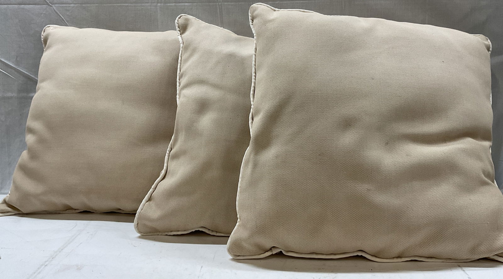Set 3 Vintage Beige Woven Outdoor Throw Pillows: Set of 3 vintage beige woven outdoor throw pillows. Woven fabric texture and piping around the edges. Measures approx 19 x 19 inches. Surface wear consistent with exposure. Blemishes observed. Throw p