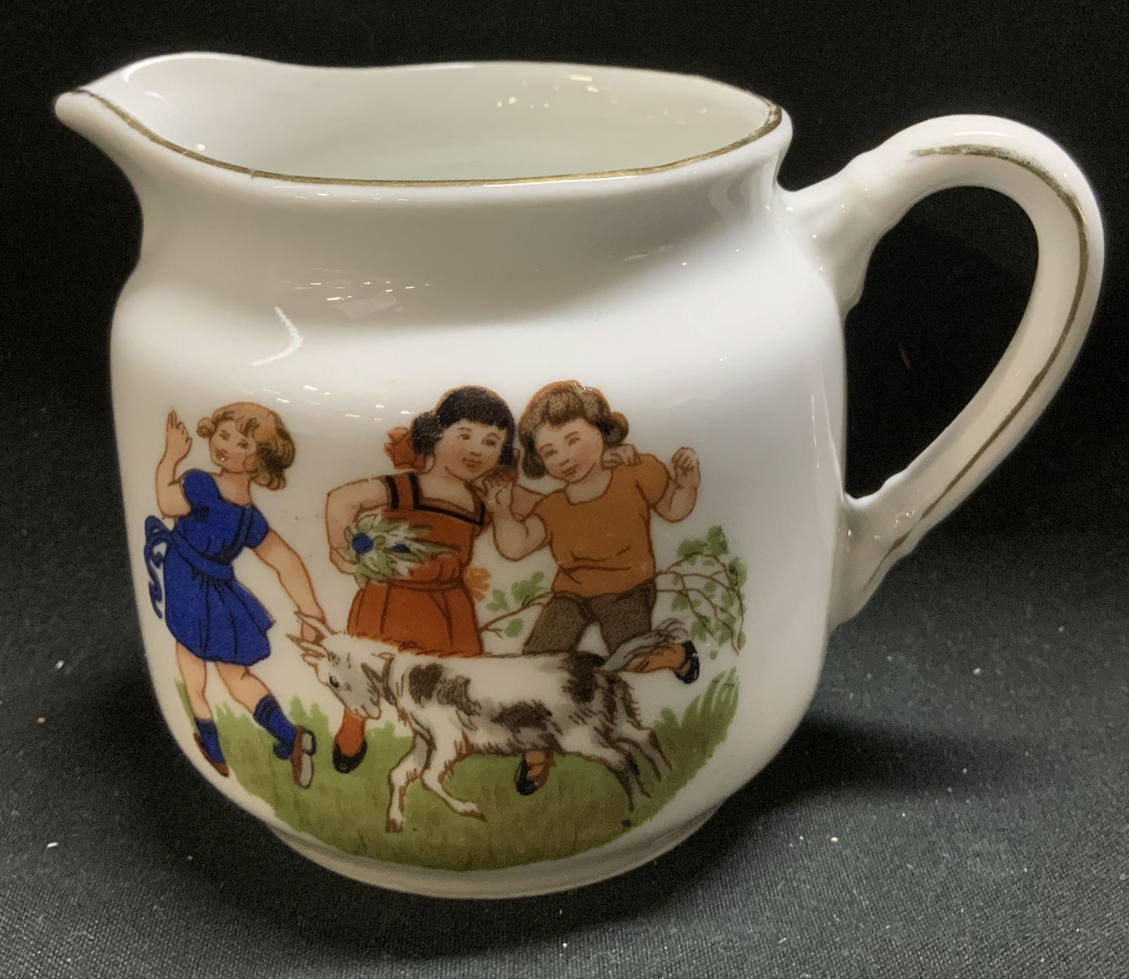 Antique Children at Play Porcelain Creamer GERMANY: Antique porcelain creamer features 3 children playing with a goat & bird motifs. Gilt accents on rim. Signed & marked on underside. Read, OG GERMANY. Surface wear consistent to age, use & exposure. Me