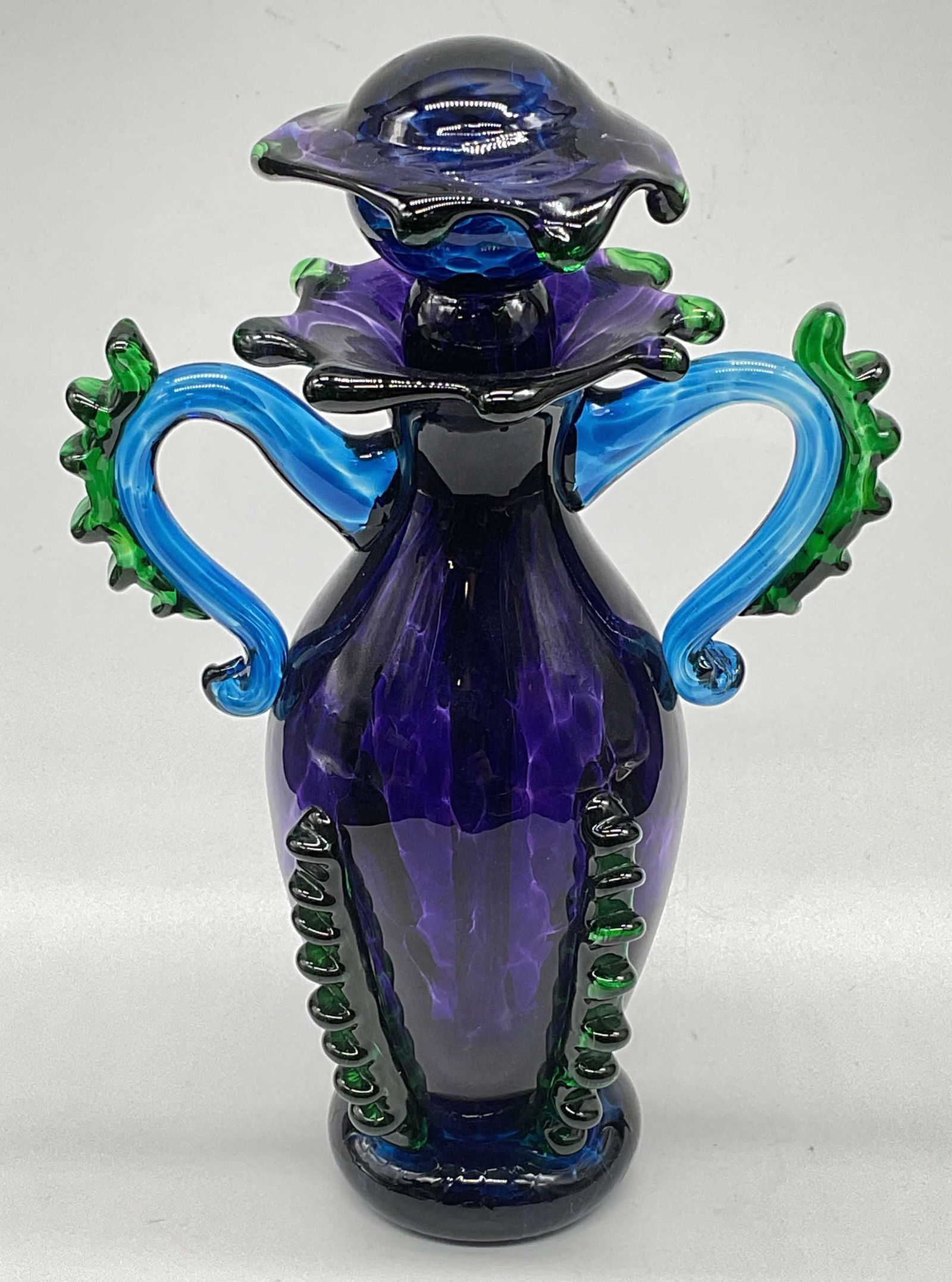Signed Art Glass Ruffle Perfume Bottle: Signed hand blown art glass perfume bottle. Applied ruffle decoration with scalloped rim and stopper. Amethyst purple with blue and green. Signed illegibly, dated 1996. Measures approx 4.25 x 6.75 inc