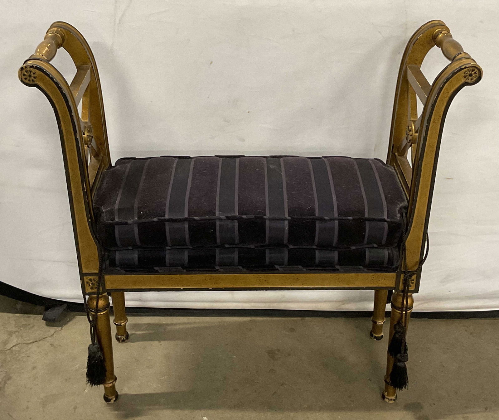 French Style Gilt Wood Upholstered Bench: French style gilt wood bench. Curved arms with carved detail. Gilt and painted black. Striped purple upholstered cushion. Measures approx 28 x 8.75 x 28.5 inches. Wear including scratching and loss to