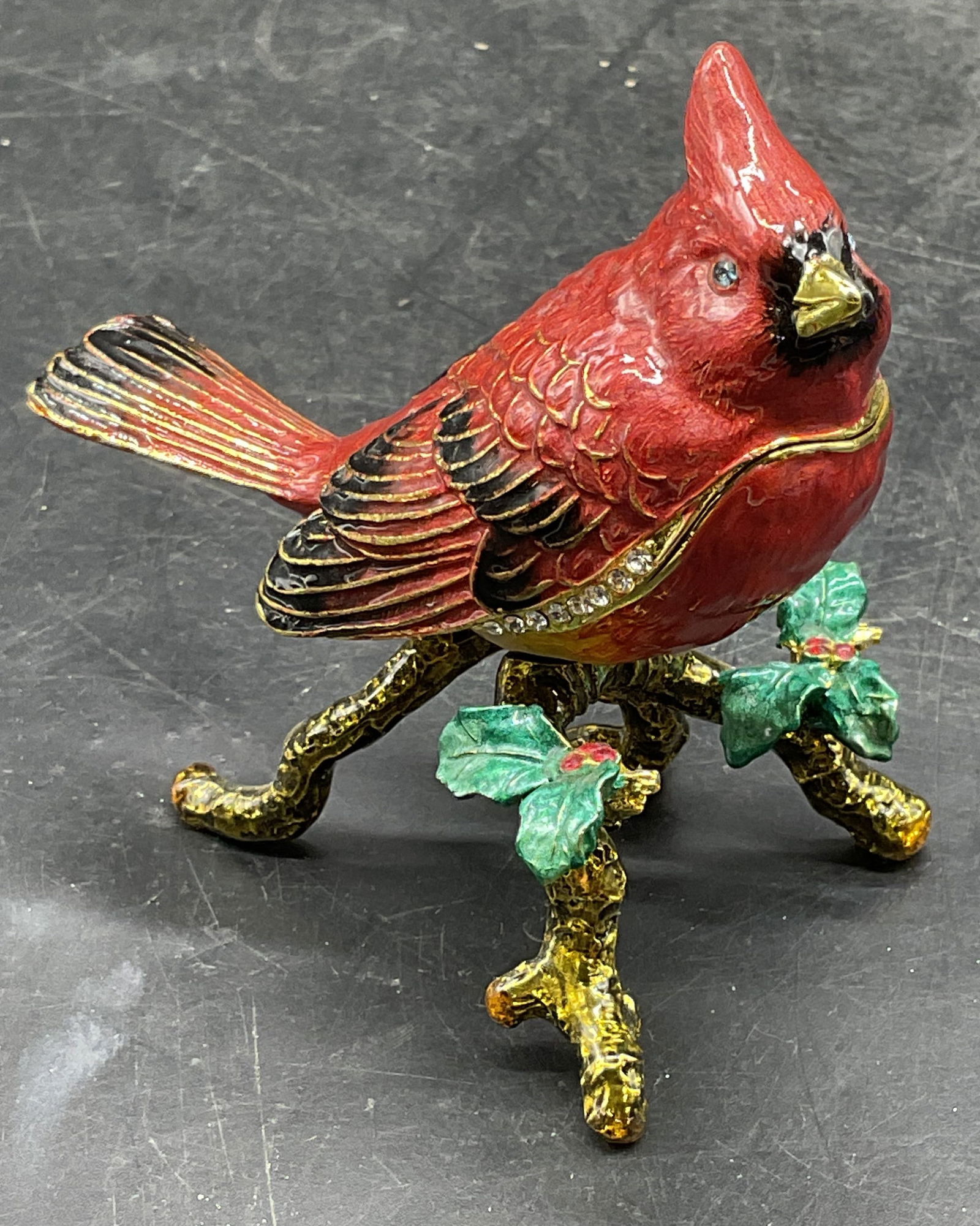 Signed Enameled Crystal Cardinal Trinket Box: Signed gold tone enameled red cardinal on holly branch trinket box with crystal decoration. Signed on underside. Measures approx 3 x 2.5 x 3 inches. Some wear consistent with exposure. Cardinal trinke