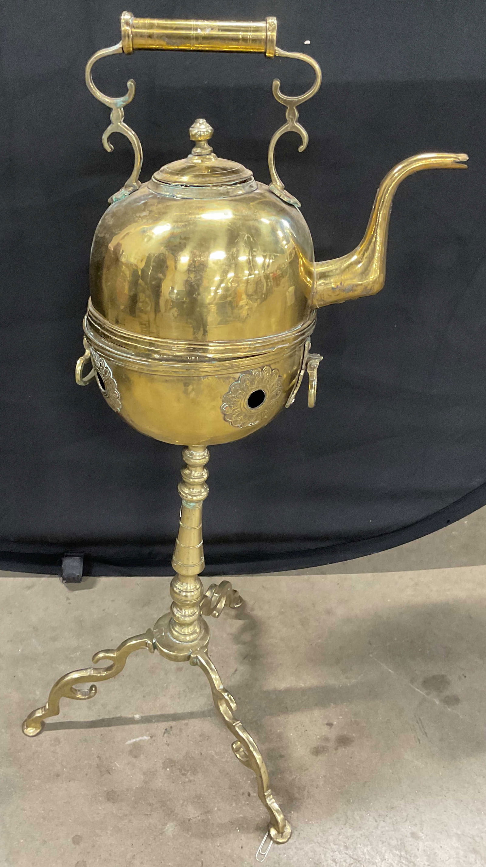 Antique Brass Standing Hot Water Kettle: Antique hot water kettle. Brass with tripod stand and kettle with handle. Decorative scroll and floral design. Measures approx 14.5 inches wide at base, 34 inches tall. Wear including warping and scra