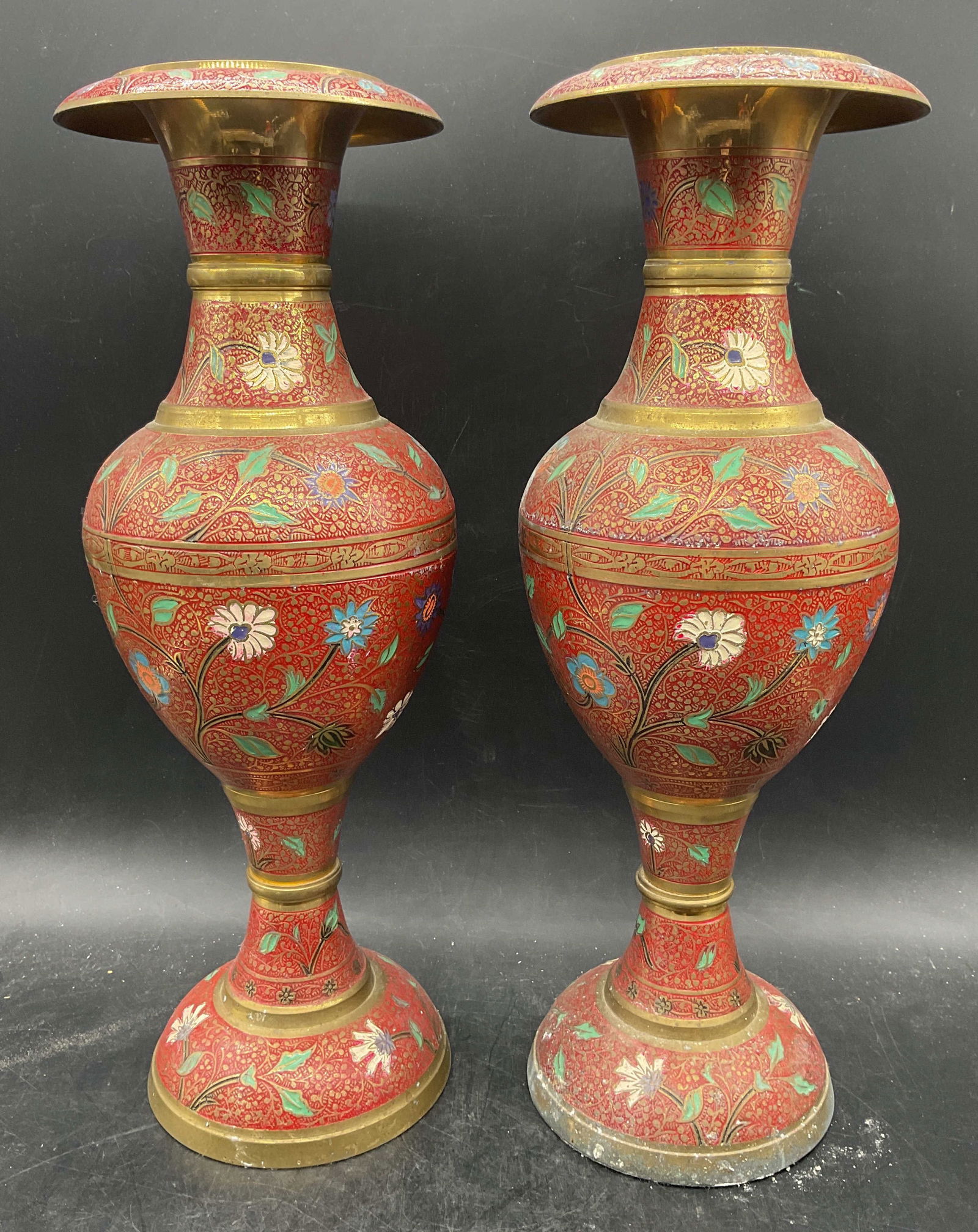 Pair Enameled Red Brass Floral Vases: Pair of brass enameled pedestal urn vases. Red, blue, green enamel with ornate floral design. Measure approx 5.5 x 15.5 inches. Wear including patina and scratching. Enamel vase, brass vase, urn