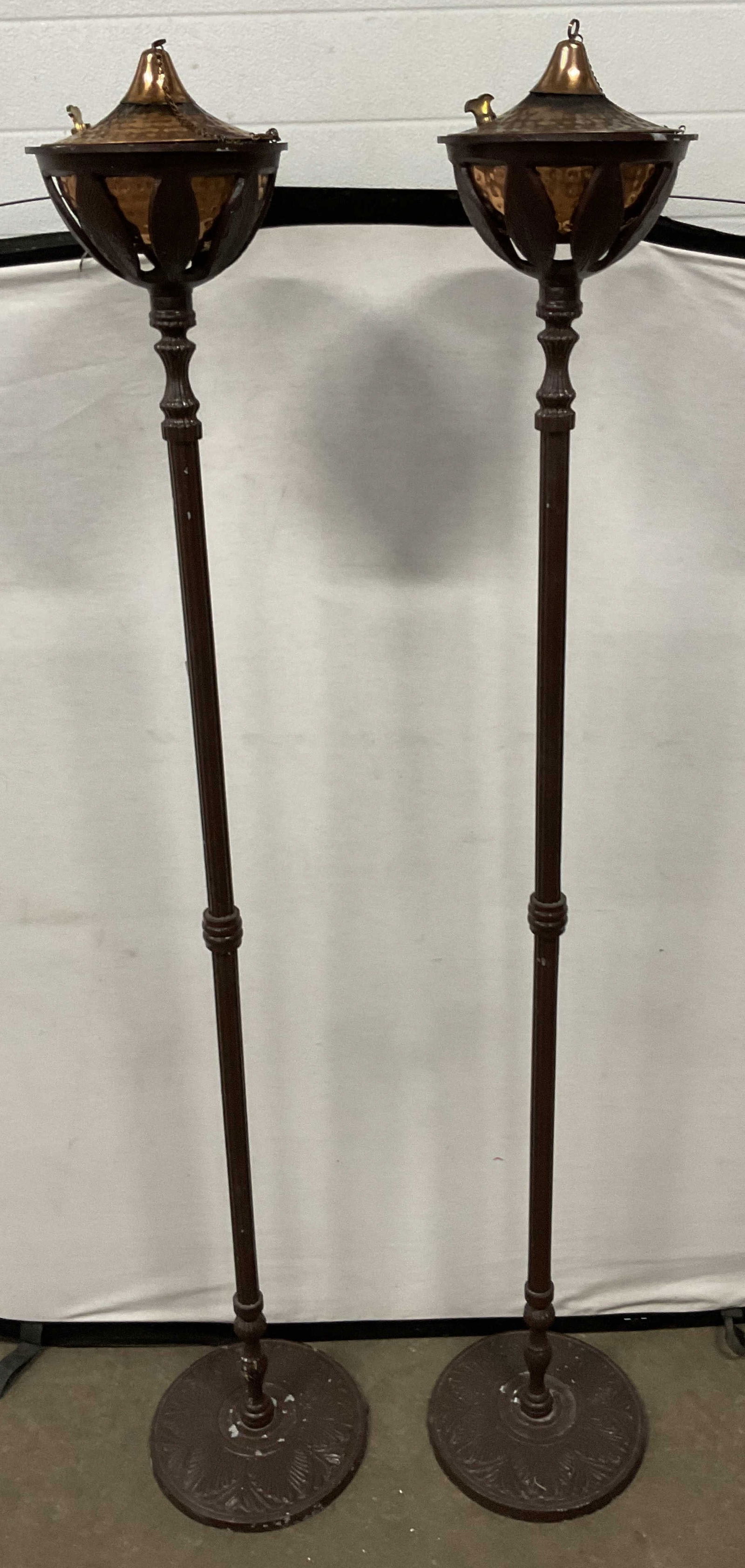 Pair Copper Brown Metal Standing Oil Lamps 64in: Pair of brown painted metal standing oil lamps with copper bowls. Slender columns with wide round bases and decorative floral design. Measure approx 10.5 x 64 inches. Wear including scratching
