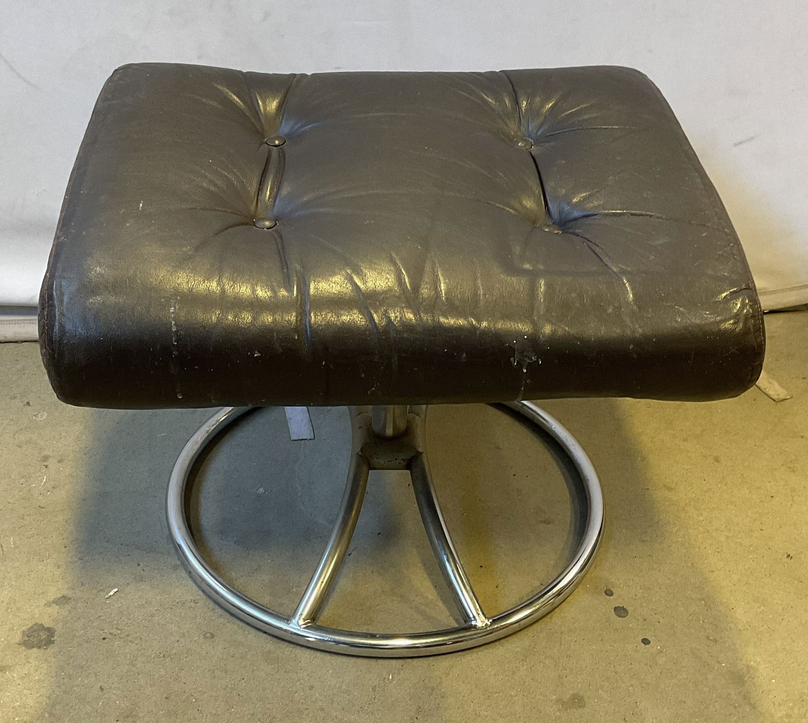 Vintage Dark Brown Leather Upholstered Ottoman: Vintage dark brown leather upholstered ottoman. Round metal spinning base. Measures approx 22 x 18 x 15 inches. Foam interior, needs replacement. Wear to leather including scratching and residue.