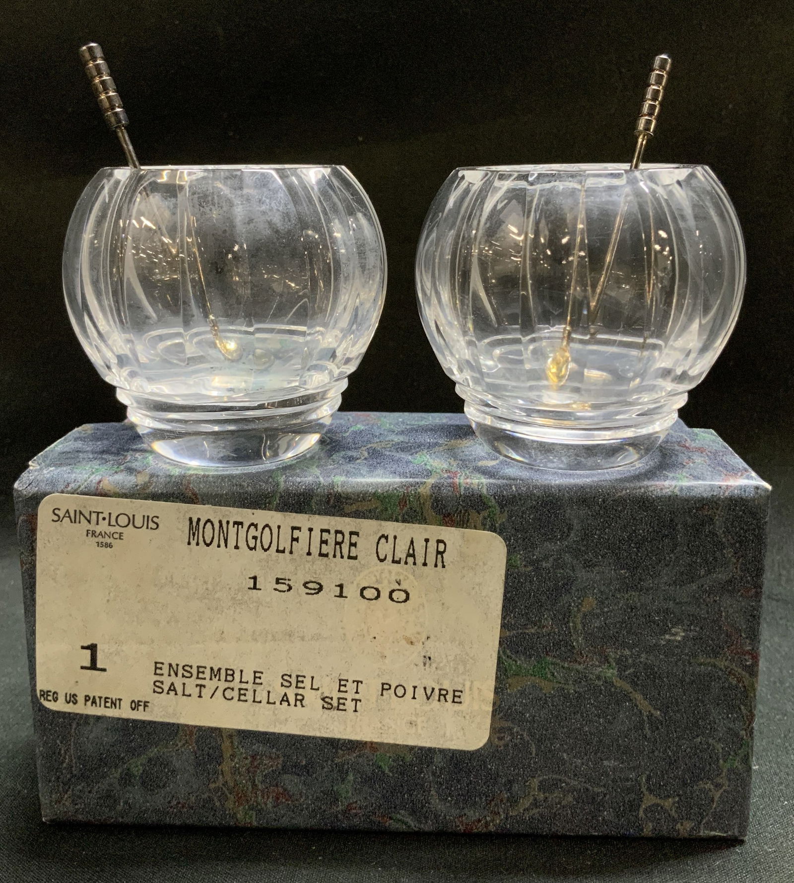 Saint Louis Montgolfiere Clair Salt Cellar Set Bx: Lot includes, Saint Louis Montgolfiere Clair salt/cellar set with miniature silver toned salt spoons. Comes with box. Cellars feature vertical fluting on body. Signed & marked on underside. Reads, ST