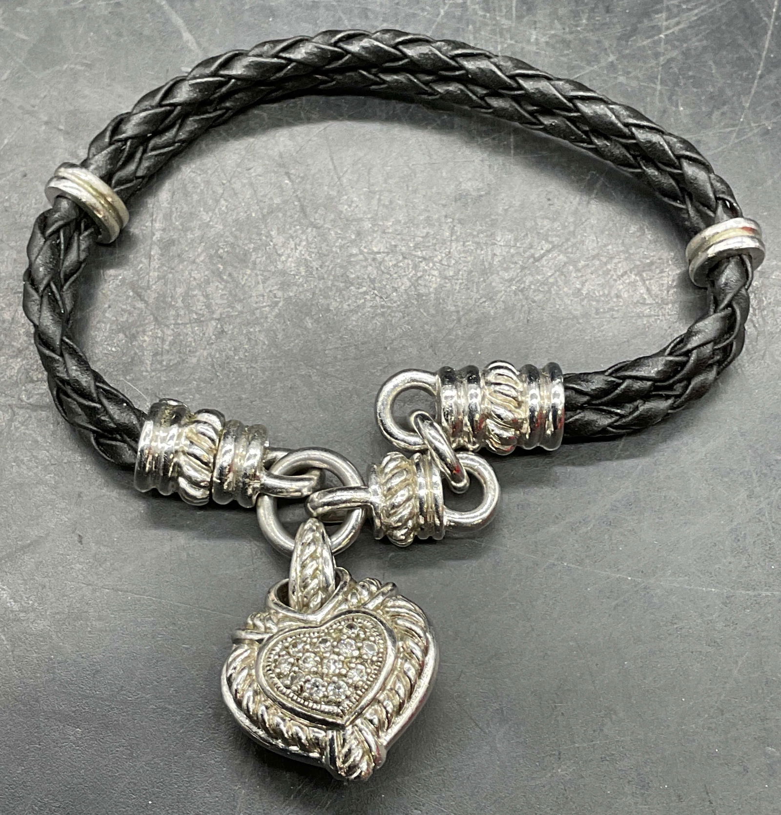 Judith Ripka Sterling Silver CZ Heart Bracelet: Signed Judith Ripka black braided leather bracelet with sterling silver accents. Heart shaped pendant with cubic zirconia. Measures approx 7 inches long. Marked sterling. Total weight 24.6 grams.
